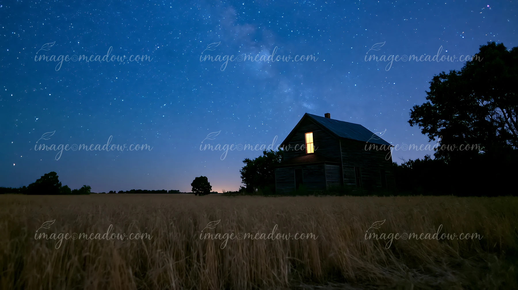 A farmhouse stands under a starry night sky, illuminated by a warm glow from its windows.