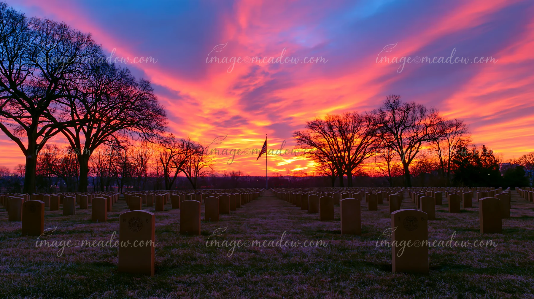 A field of headstones stretches under a colorful sunset sky with an American flag at Arlington Cemetery.