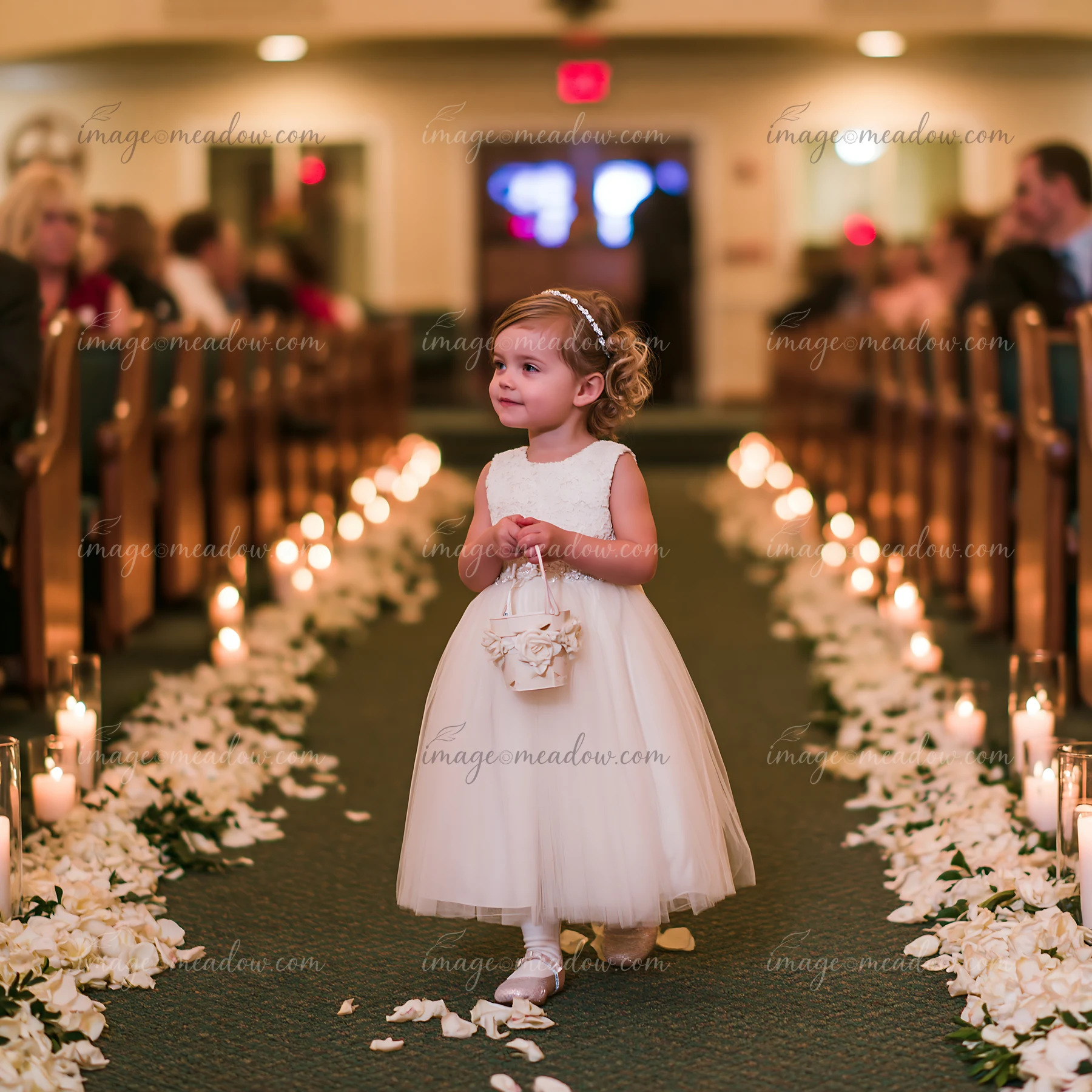 A flower girl walks down the church aisle holding a basket and spreading flower petals on the floor.