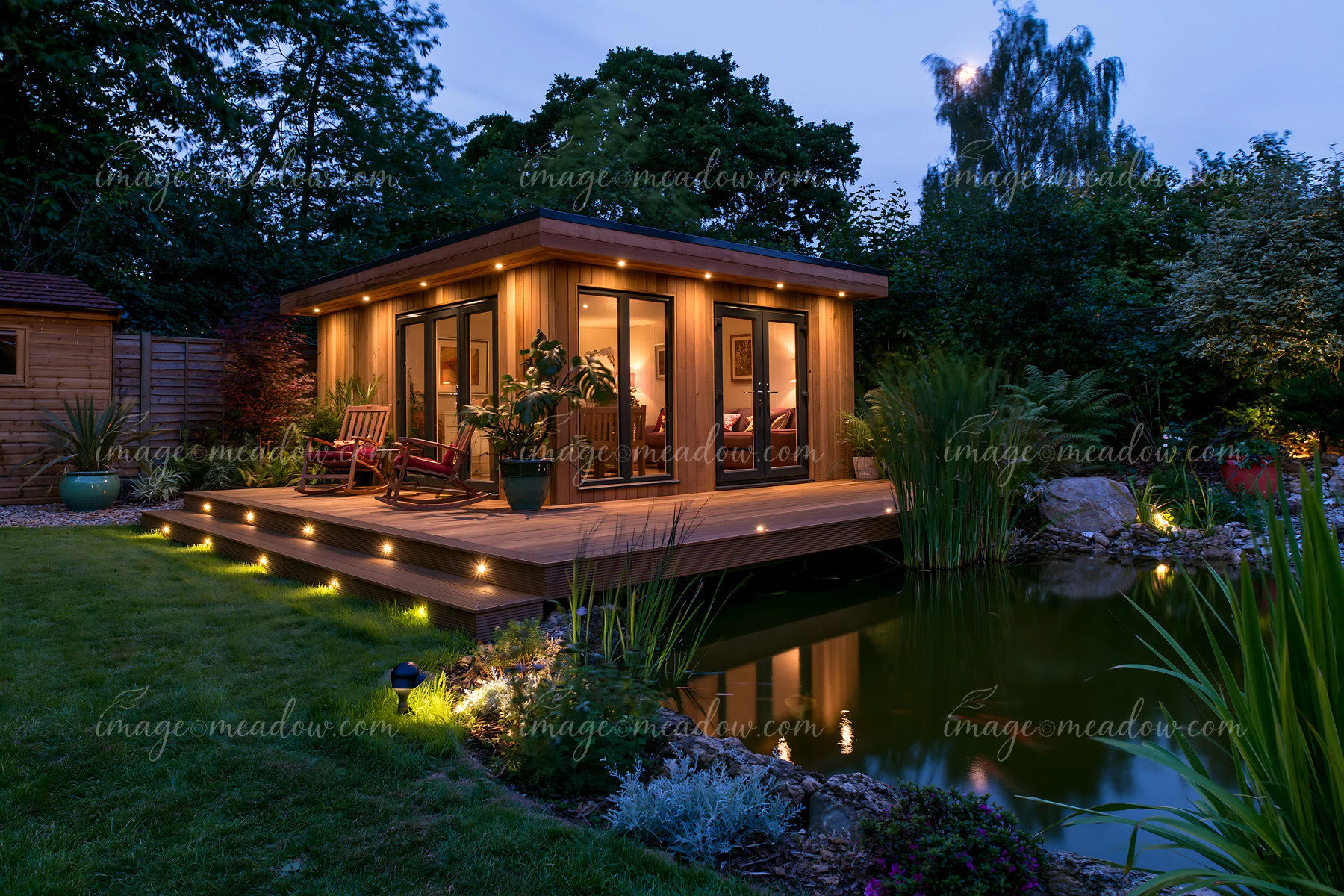 A garden room features large windows and a deck that is illuminated.
