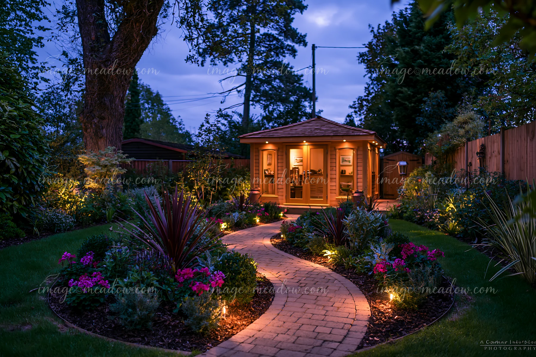 A garden studio stands empty at dusk, illuminated by pathway lights.