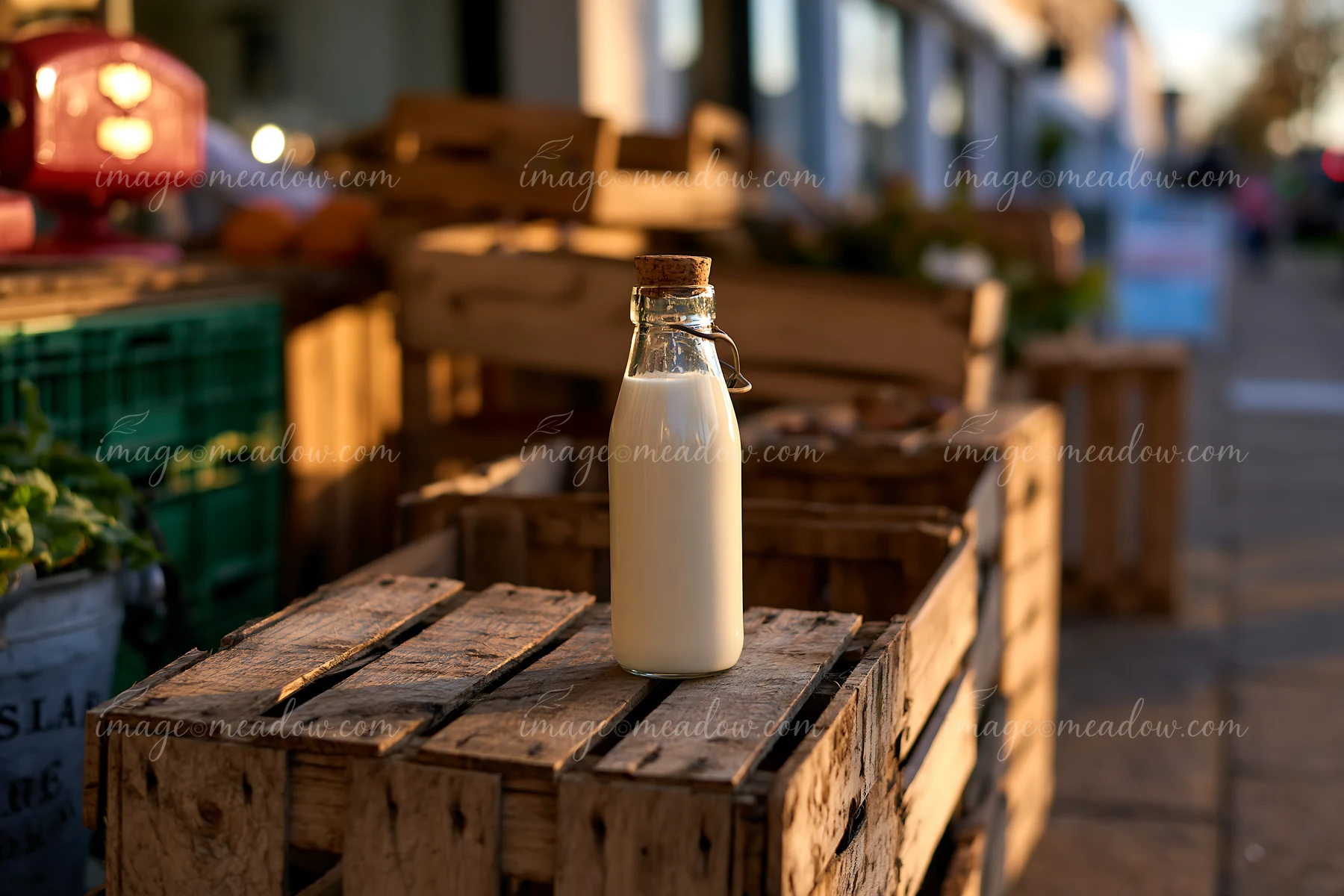 A glass bottle filled with milk stands on a wooden crate at a street market stall during golden hour.