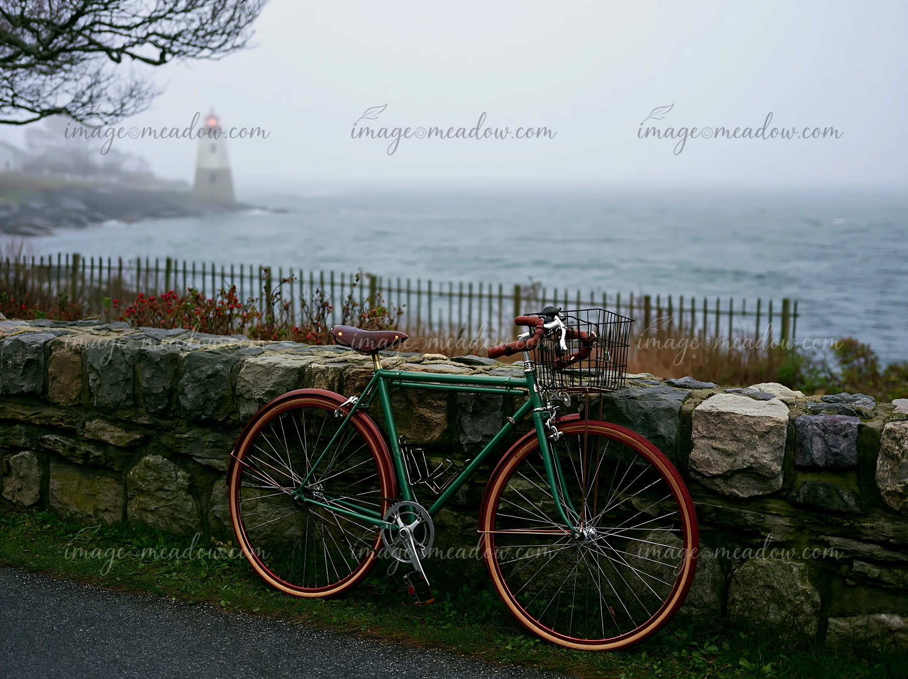 A green bicycle stands against a stone wall while a lighthouse is visible in the distance through thick ocean fog.