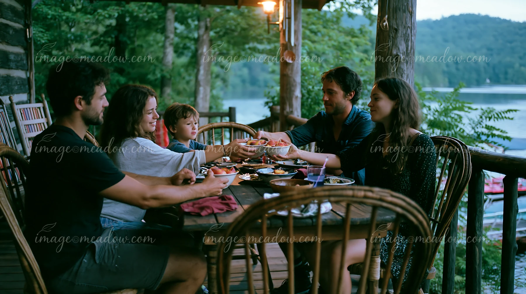 A group of five people sits around a wooden table sharing bowls of dessert after dinner at a lakeside cottage.