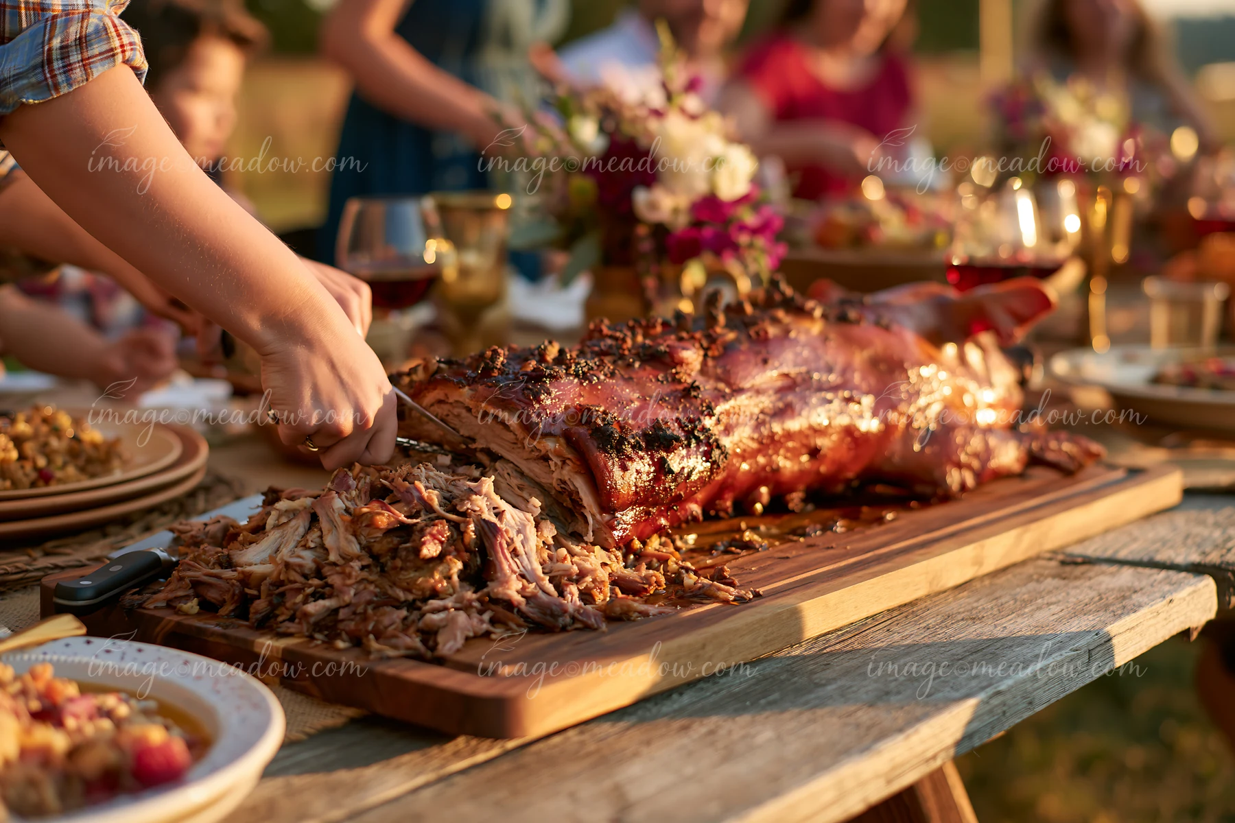 A group of people enjoy a meal outdoors with a whole roasted pig served at rustic feast on a wooden table.