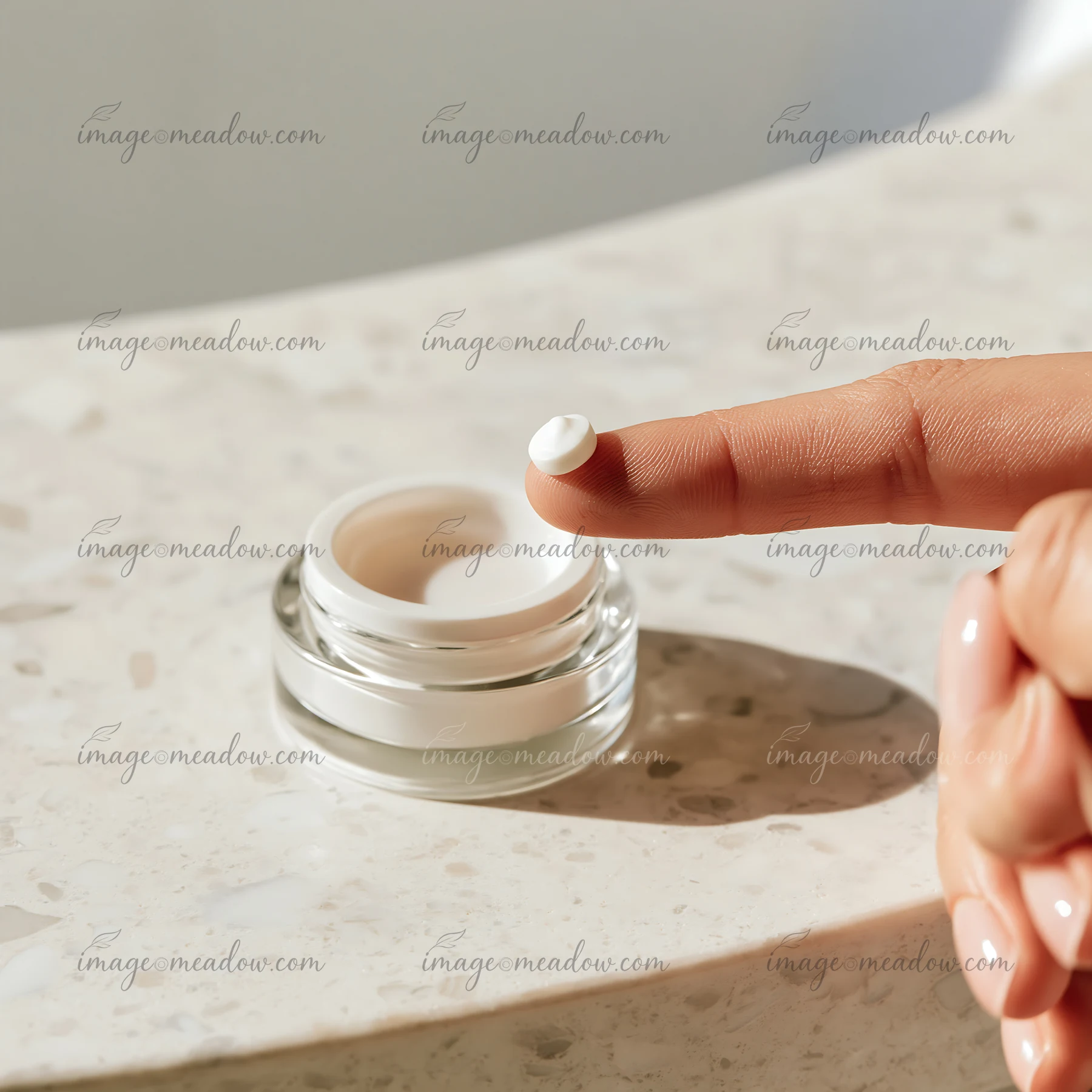 A hand holds a small amount of cream on the fingertip, ready to be applied.