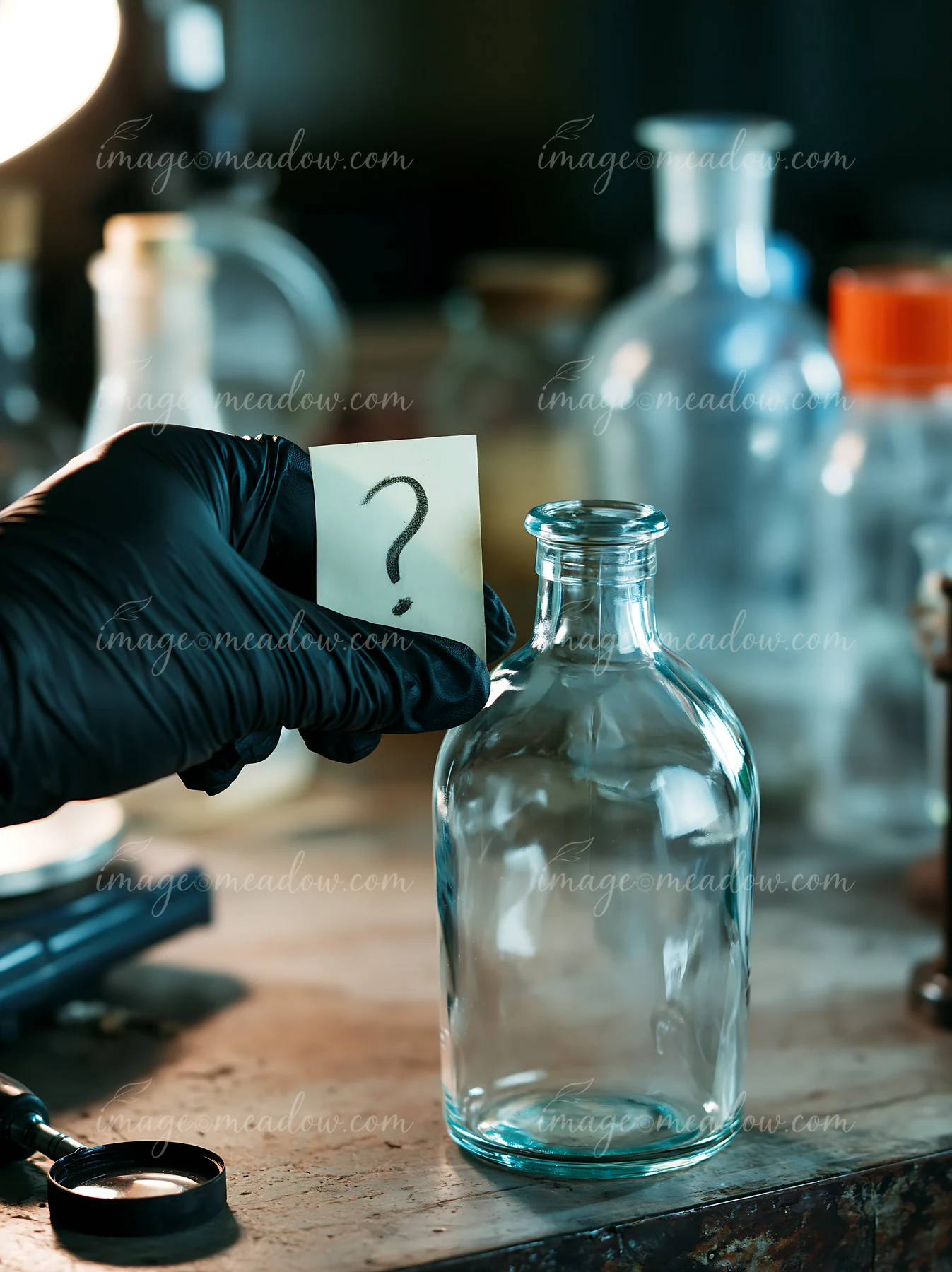 A hand in a black glove holds a note with a question mark next to an empty bottle on a cluttered workbench surrounded by other glass containers and tools.
