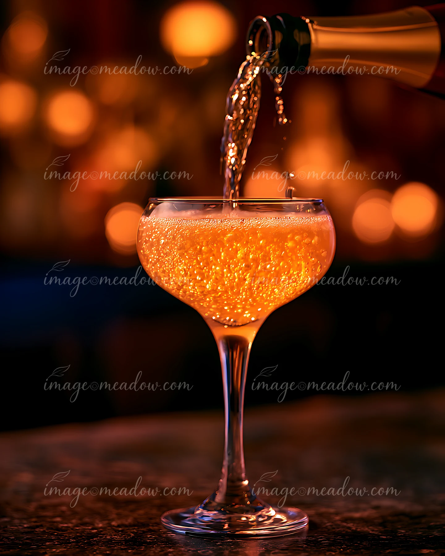 A hand pours a sparkling beverage into a clear glass at a bar with warm lighting.