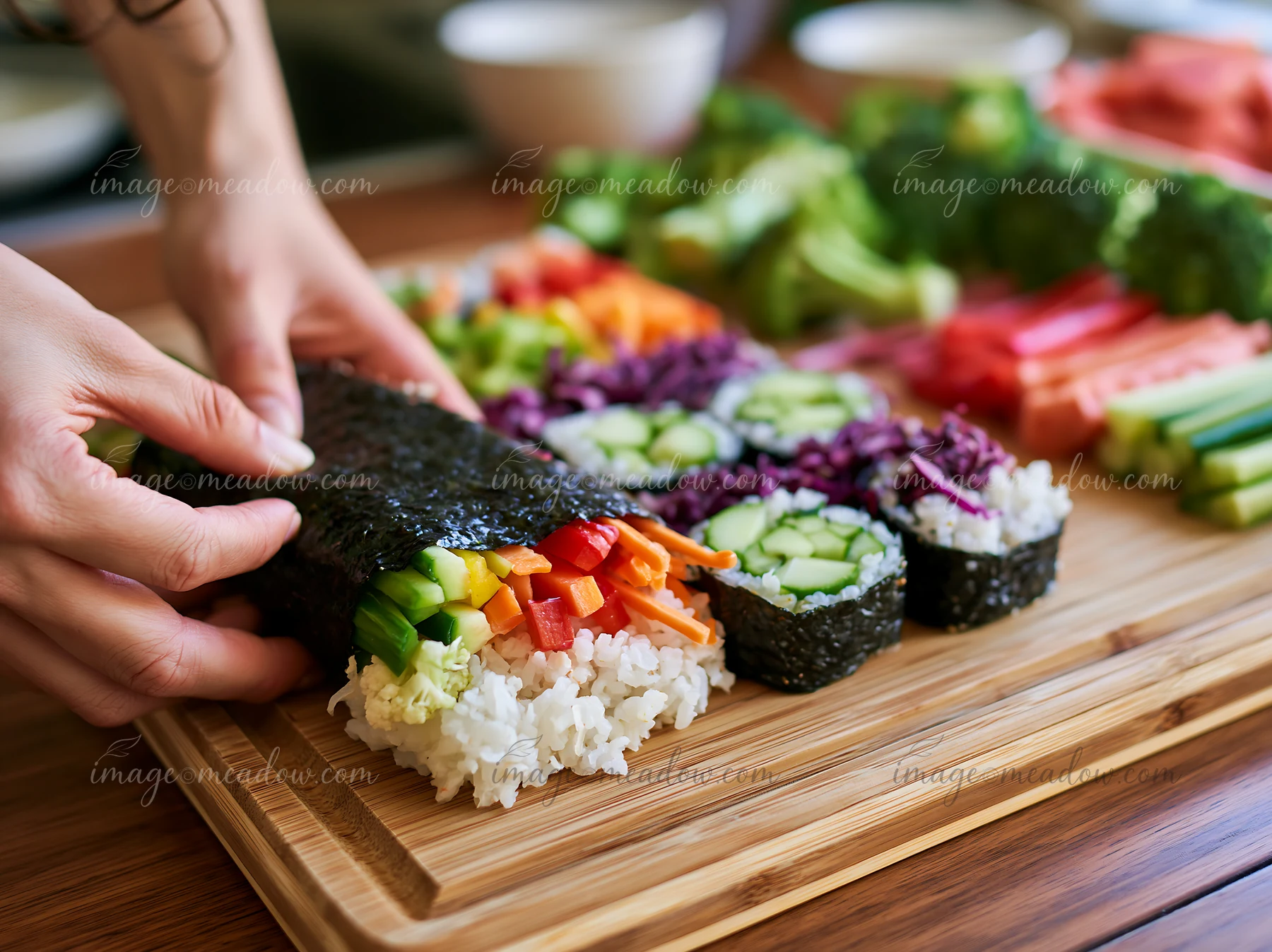 A hand rolls sushi with fresh vegetables including cucumber, bell pepper, and carrots on a wooden cutting board.