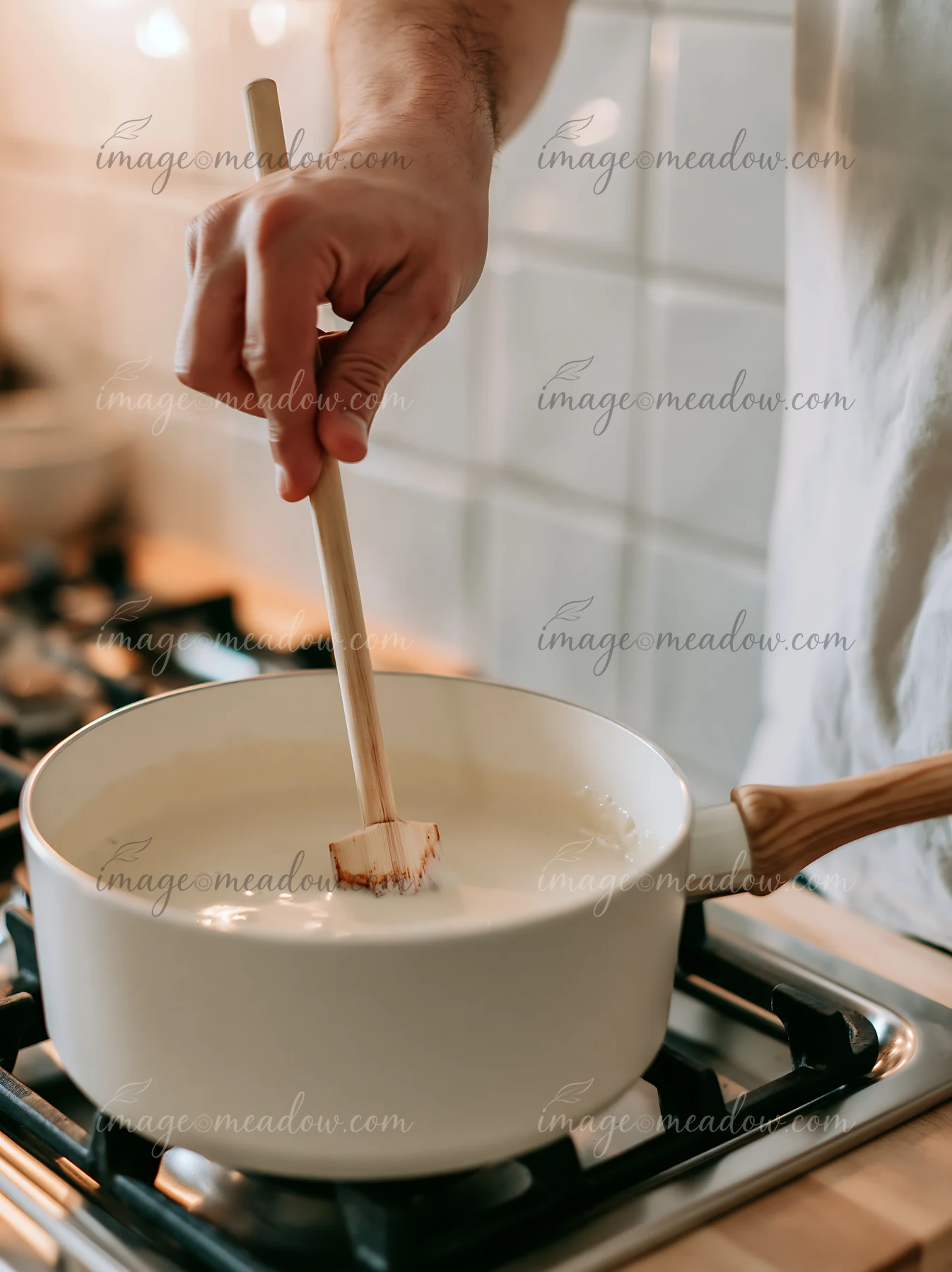 A hand stirs cream with vanilla pods in a pot on a stovetop.
