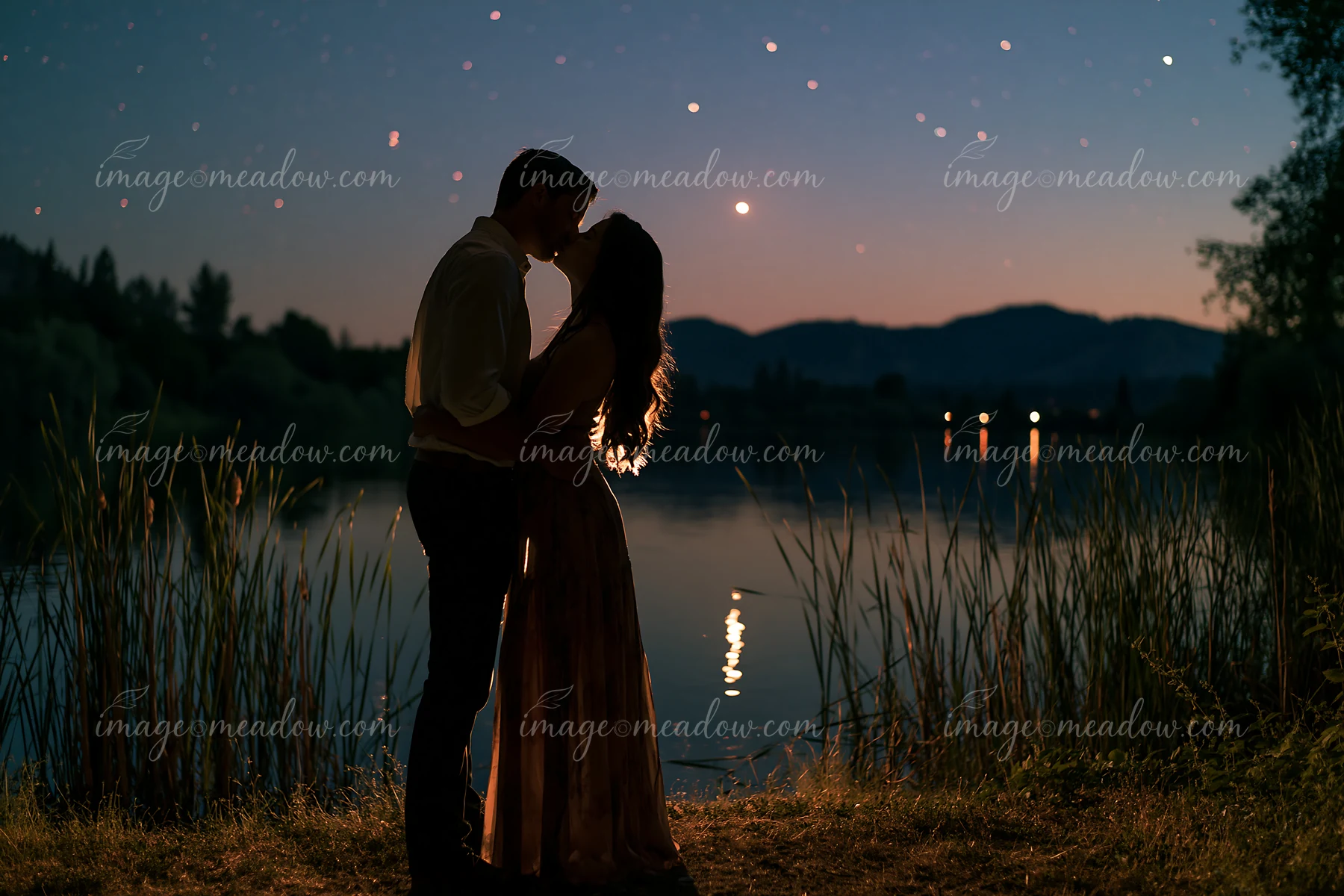 A happy couple kissing beneath stars in nature beside a calm lake.