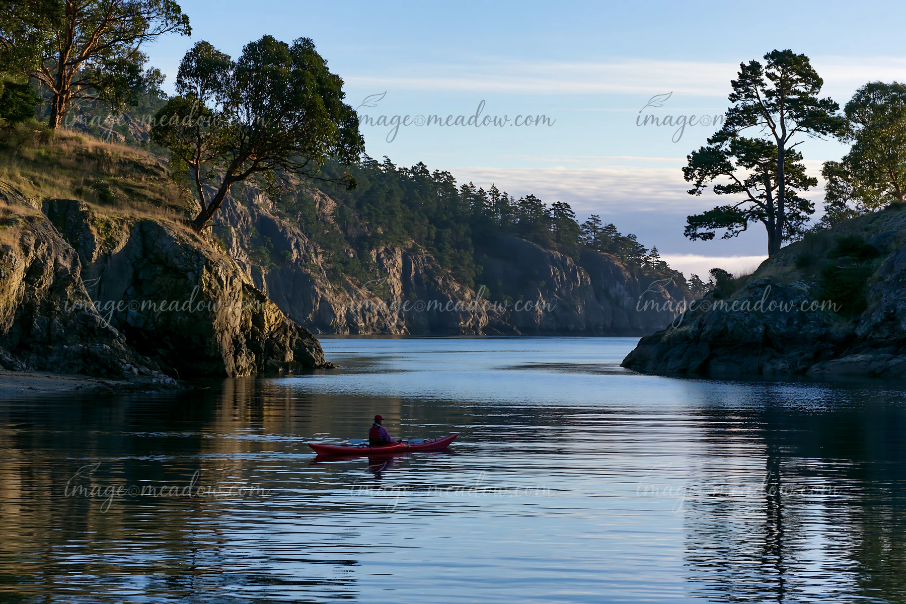A kayaker moves through calm waters in a sheltered bay, flanked by cliffs and trees.