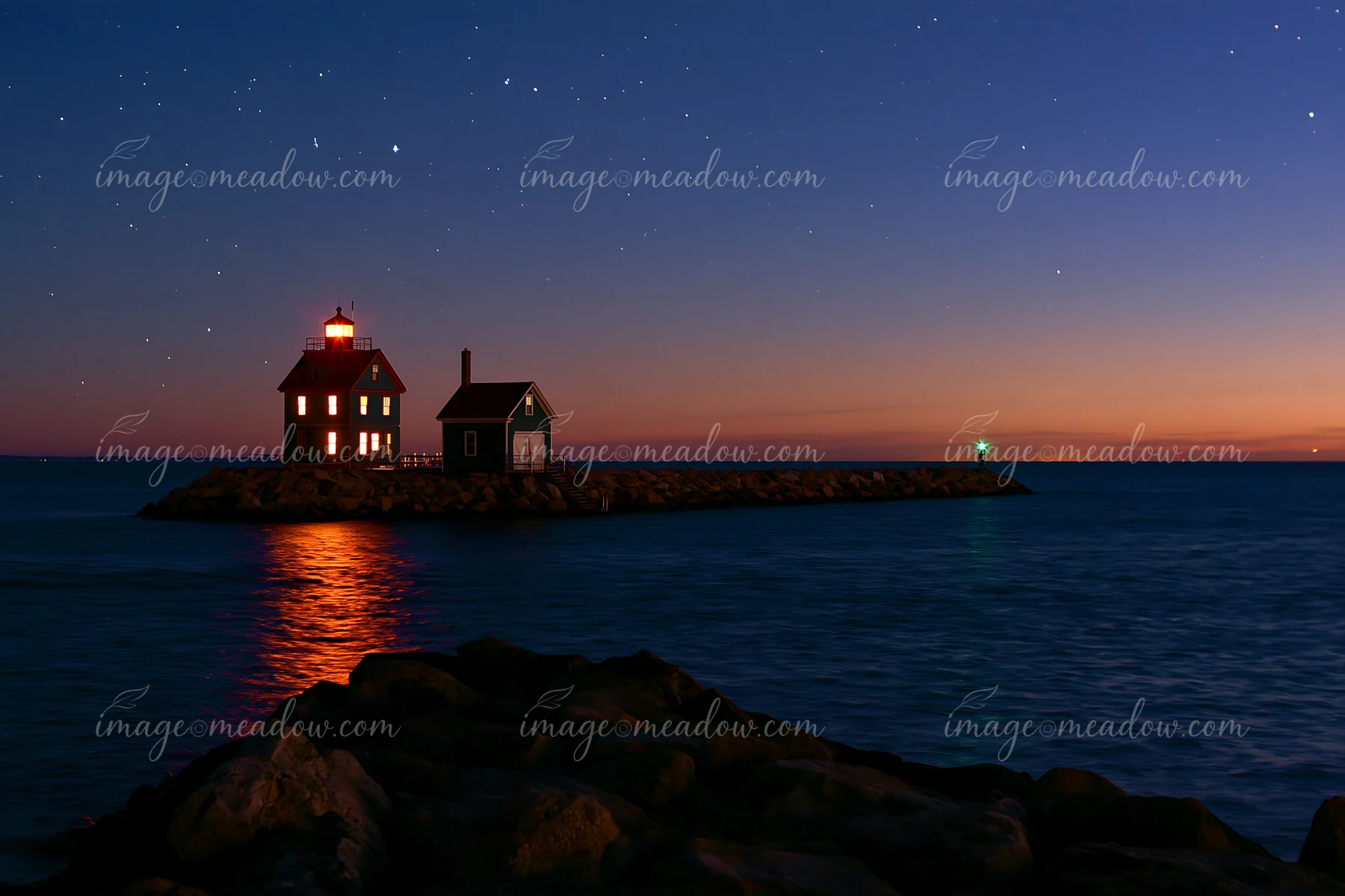 A lighthouse house under stars stands on a rocky jetty at dusk, with a calm sea reflecting the lights.