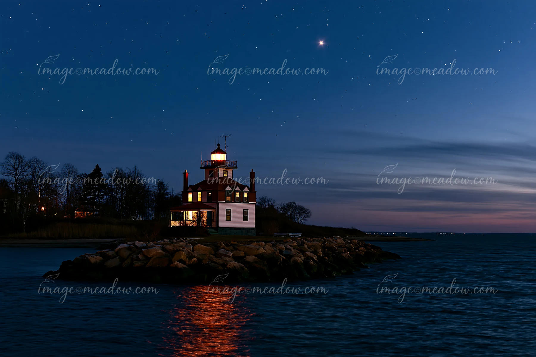 A lighthouse house under stars stands on a rocky shore at night.