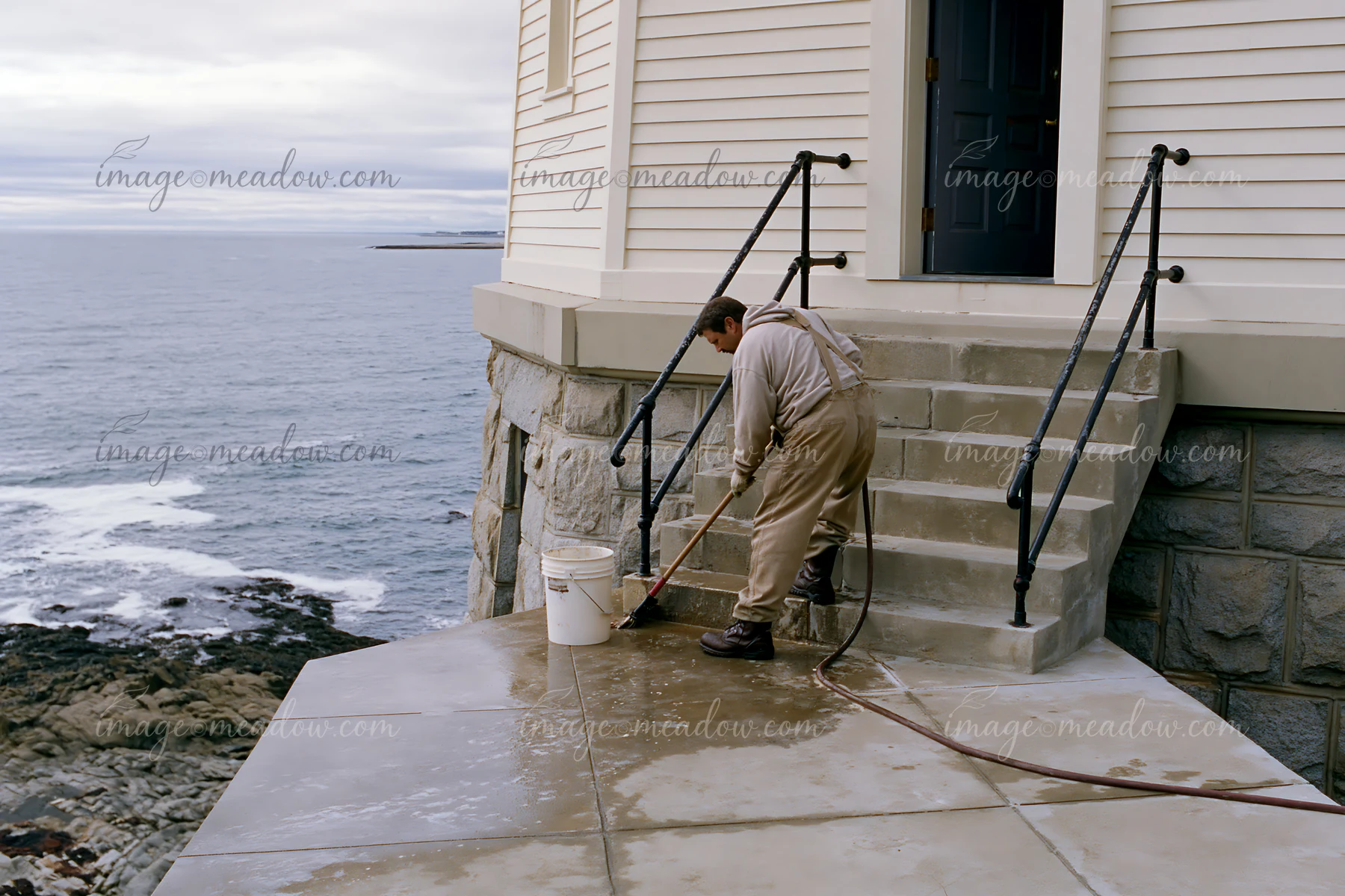 A lighthouse maintenance worker at work cleans the stone steps leading to the water.