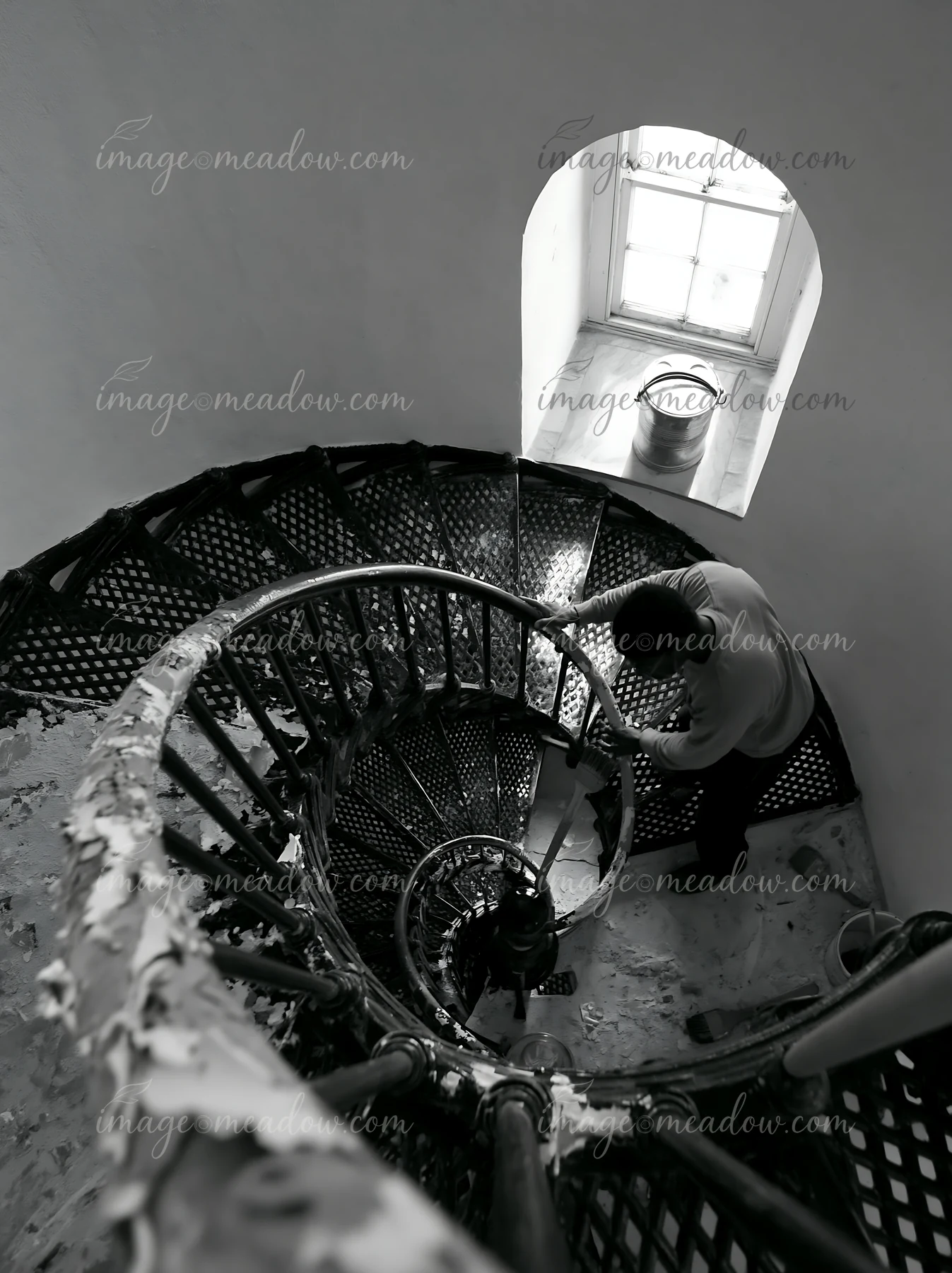 A lighthouse maintenance worker at work repairs equipment while standing on a spiral staircase.