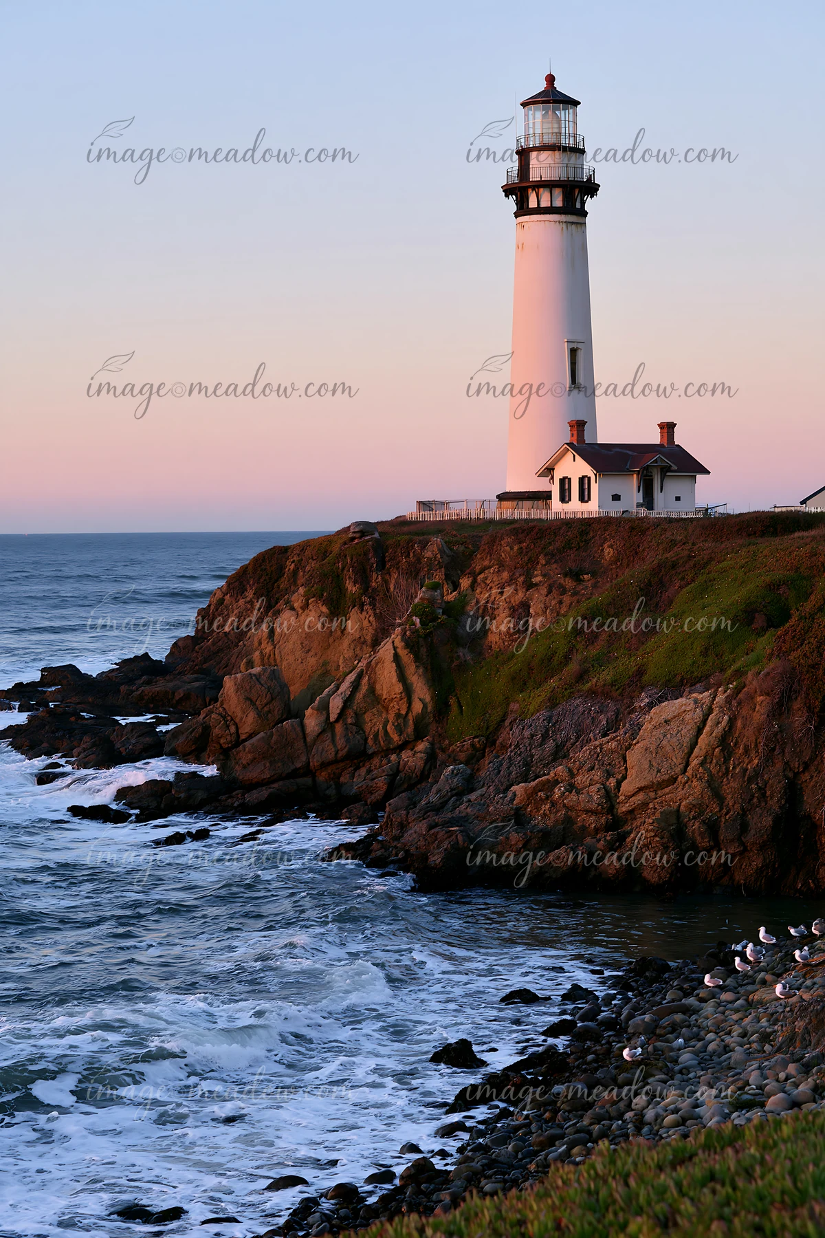 A lighthouse stands on a rocky cliff near a tide pool with waves crashing against the shore.