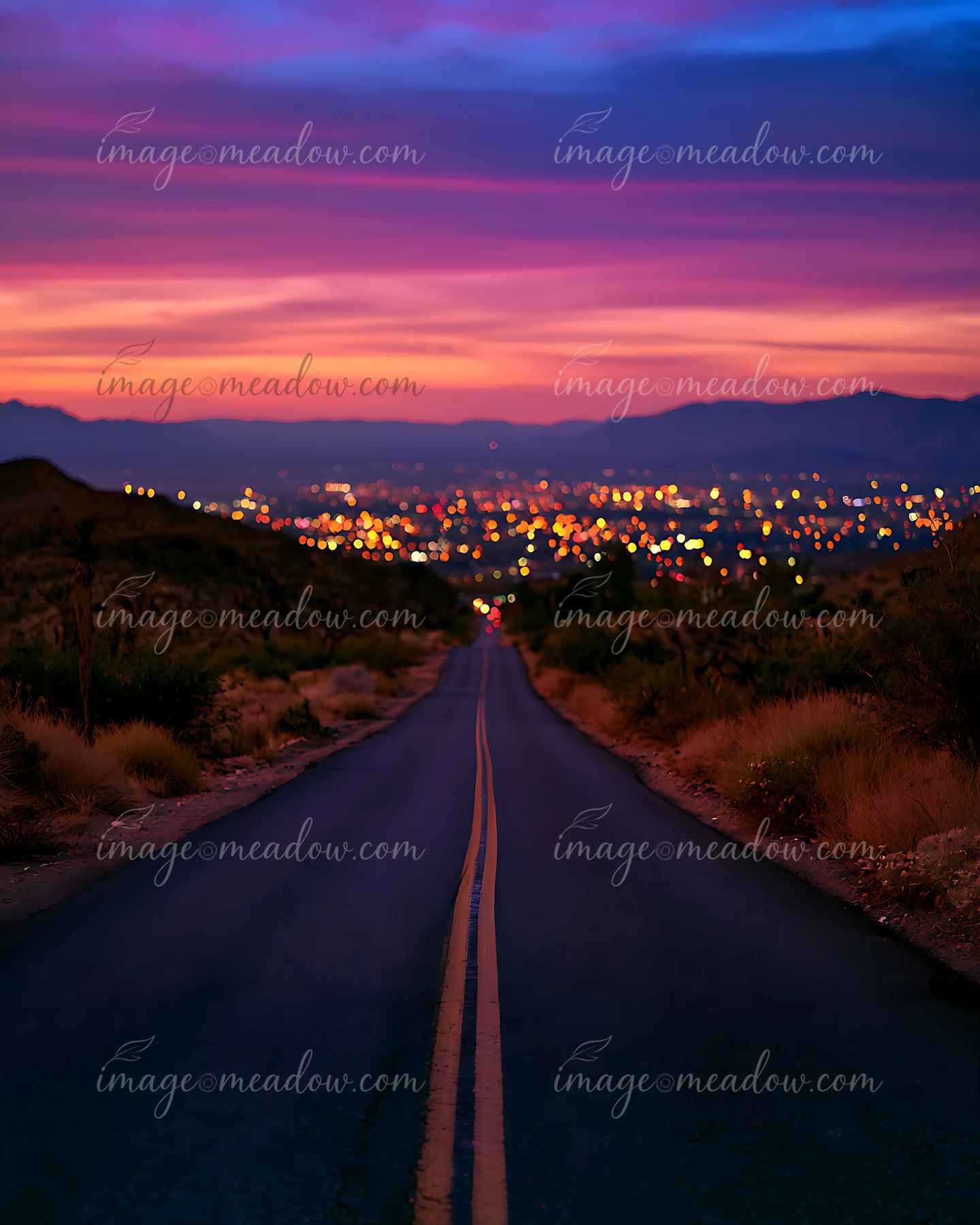 A long road stretches toward a city at dusk, illuminated by numerous lights.