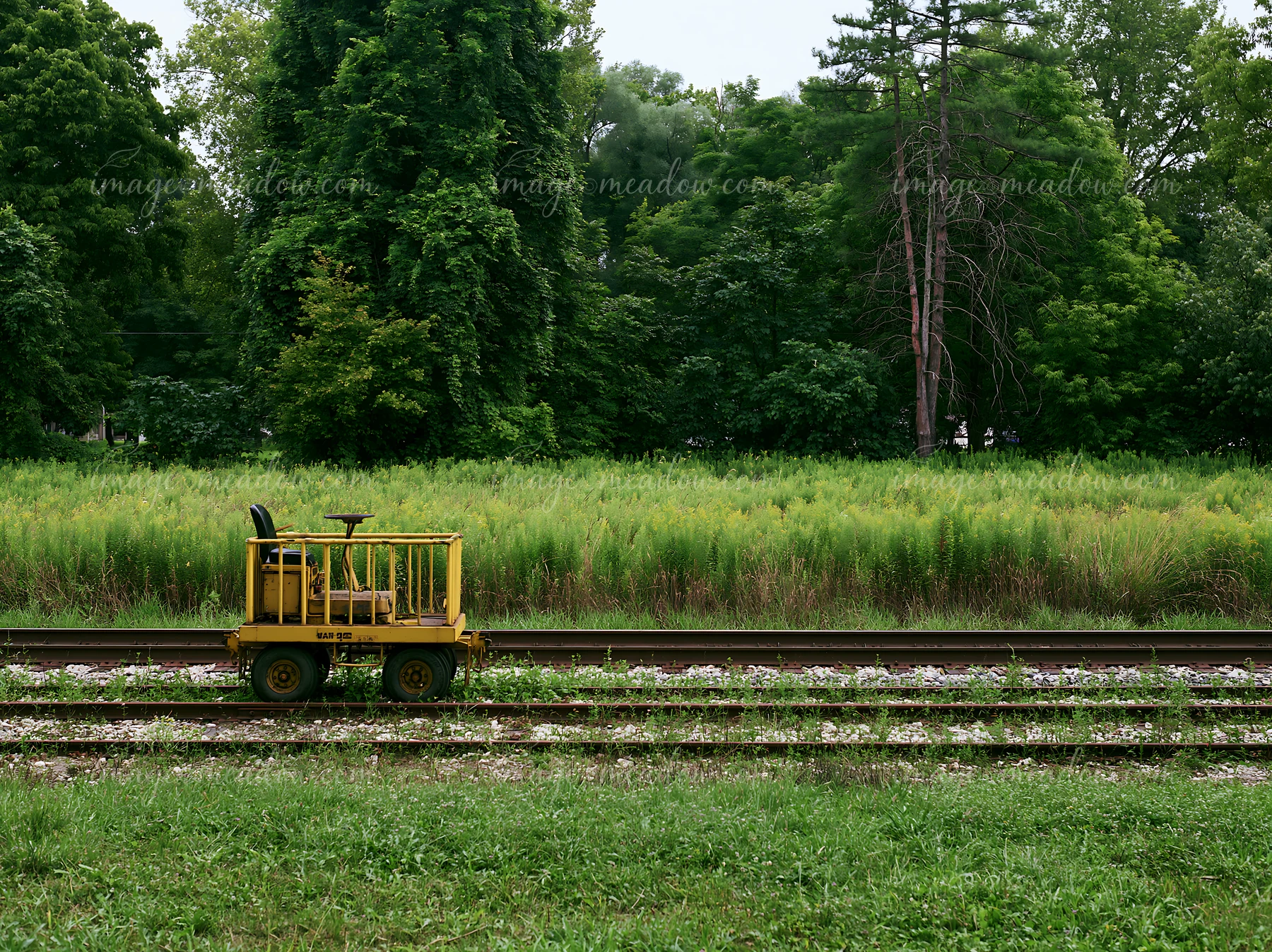 A maintenance cart sits on railway tracks next to a meadow alongside railway tracks.