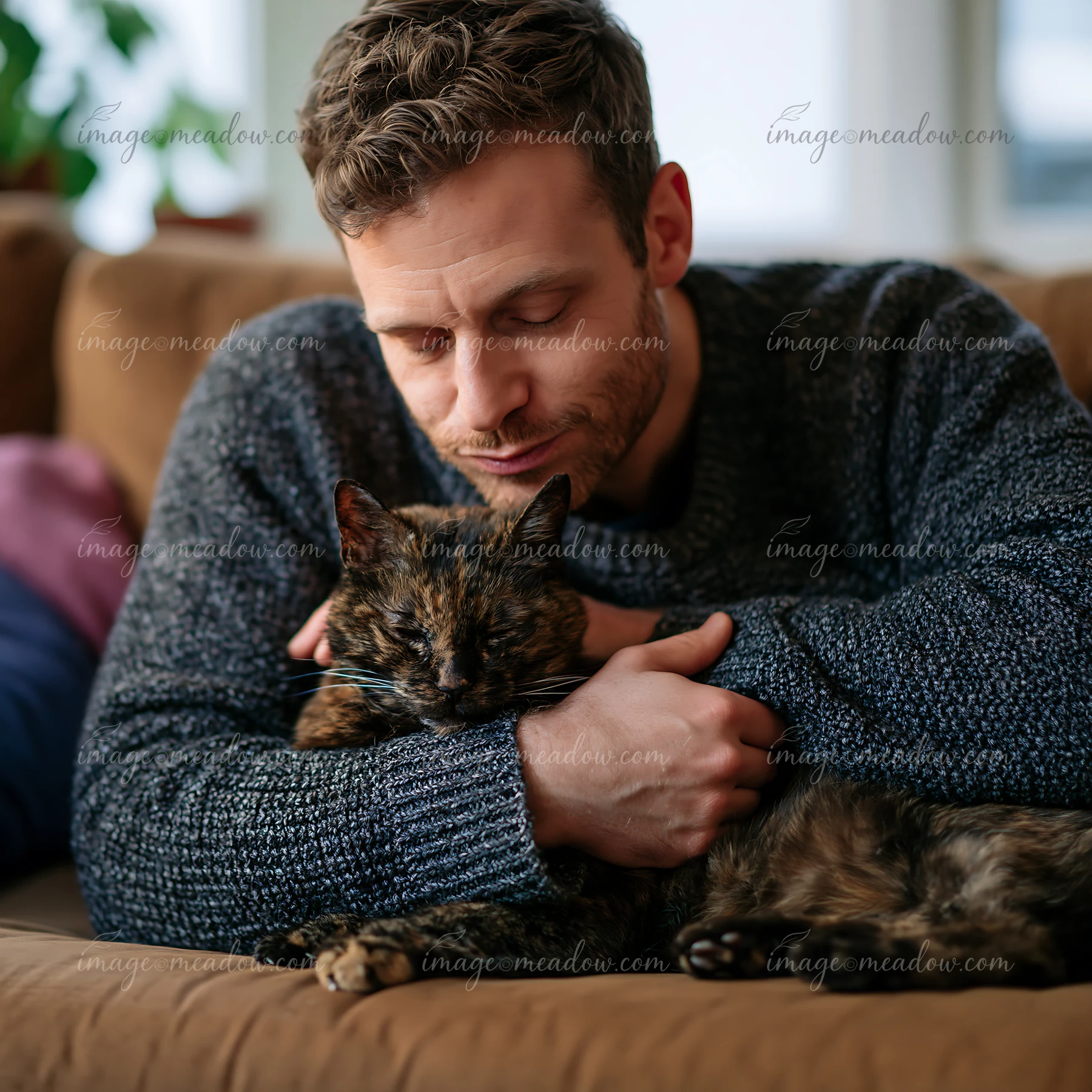 A man holds a cat in his arms while sitting on a sofa in a cozy living room.