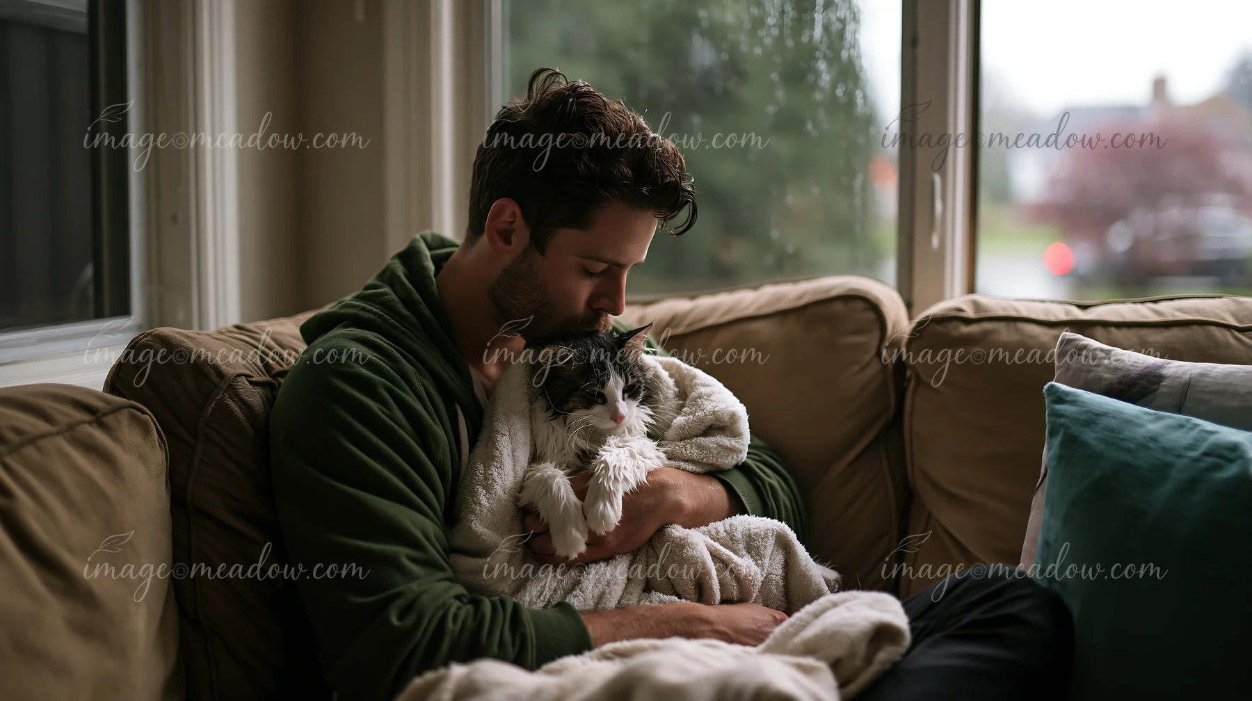 A man is sitting on a sofa, holding a cat, and gently kissing it.