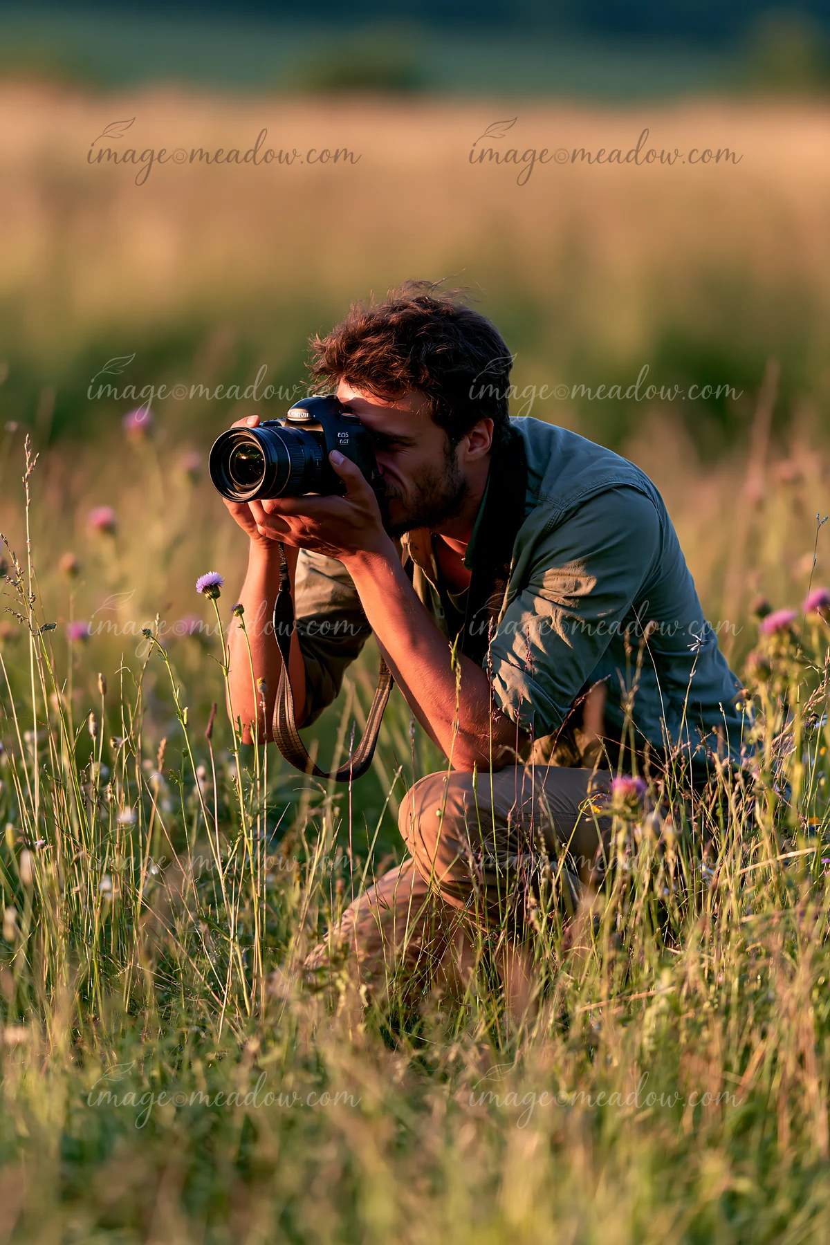 A man kneels in a field, capturing photos of blooming meadow flowers as the sun sets in the background.