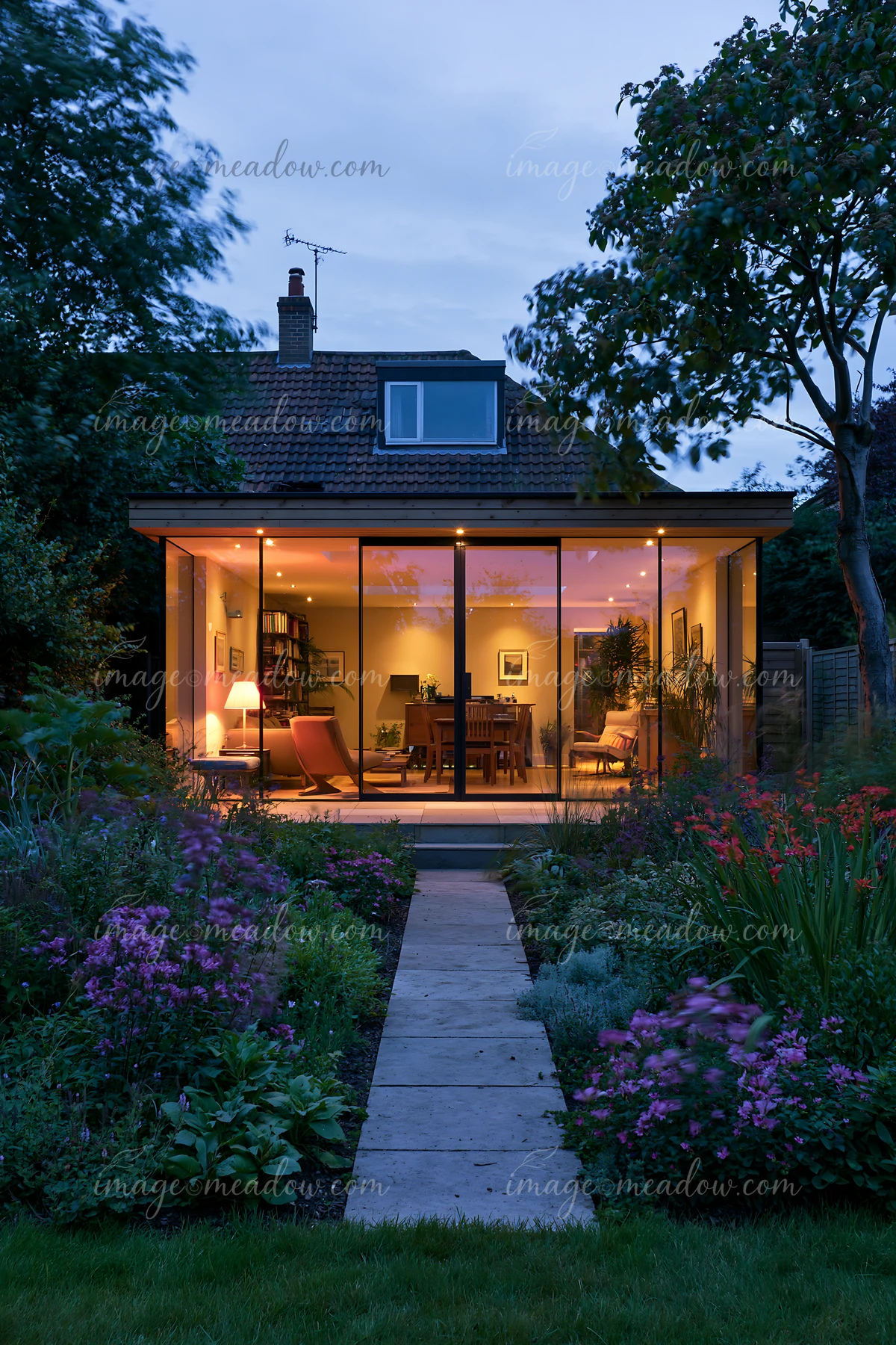 A modern empty garden house with glowing glass walls showcases a well-lit interior filled with furniture.