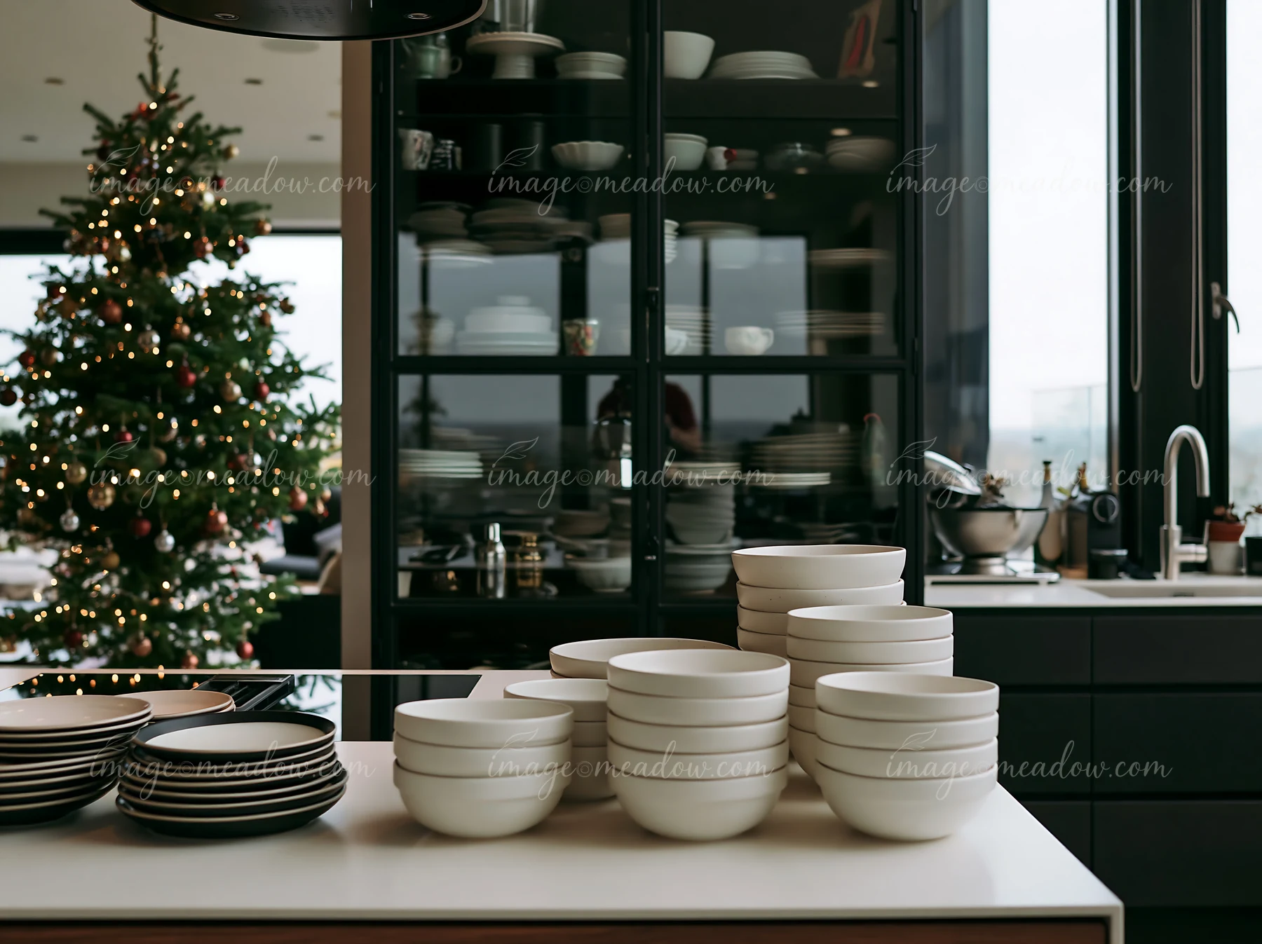 A modern kitchen features a large Christmas tree reflected in the glass cabinet.