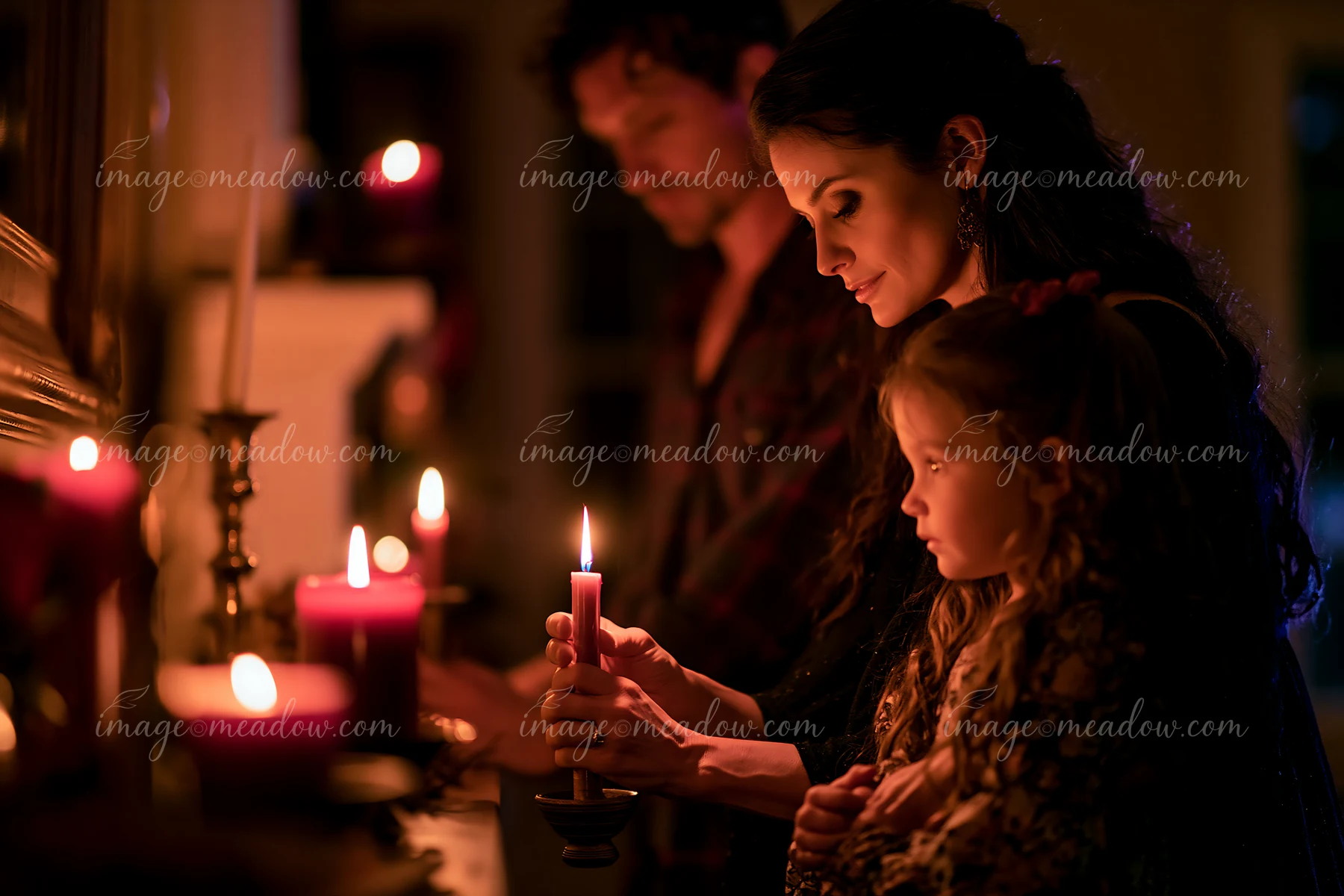 A mother and father help their daughter with a candle during a holiday tradition in their home.