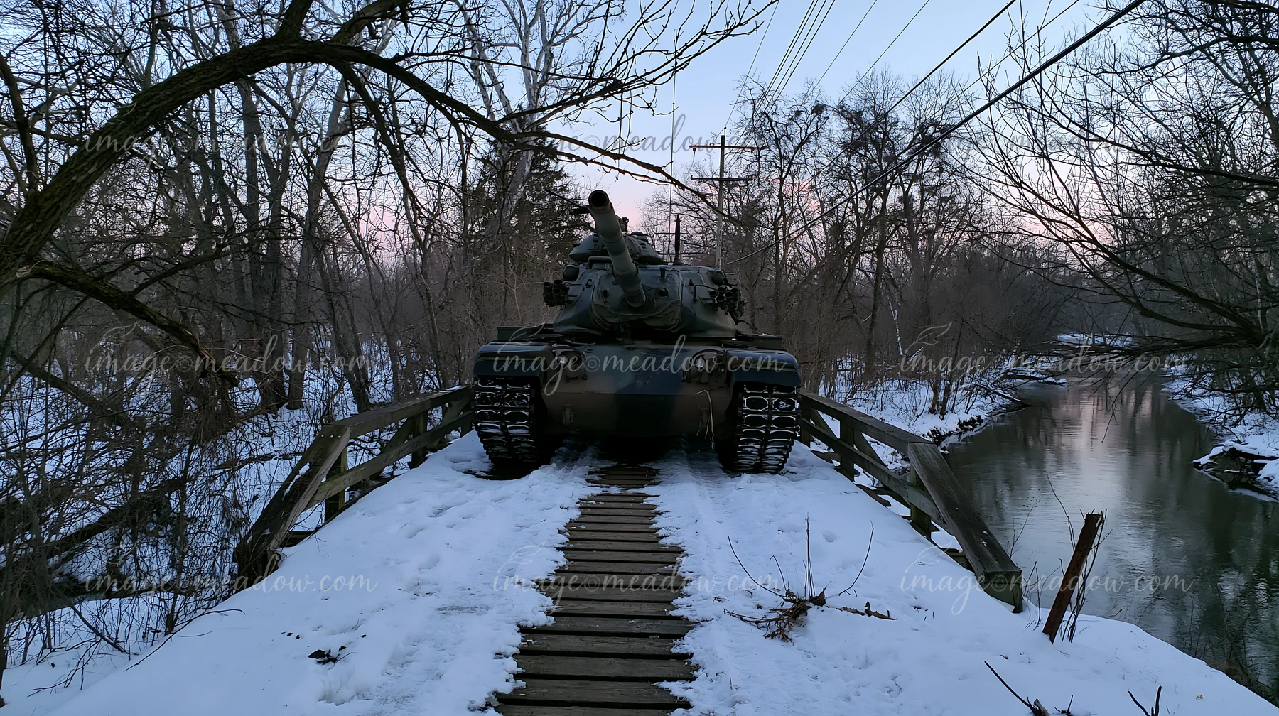 A panzer tank in winter snow sits on a wooden bridge above a creek.