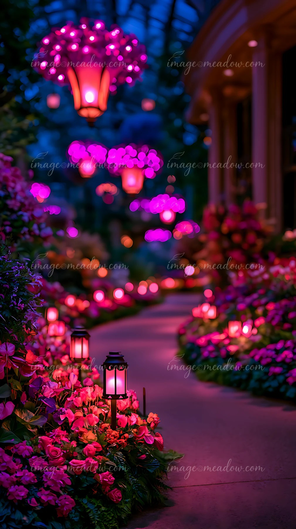 A pathway is illuminated by lanterns and surrounded by blooming flowers in a garden during the evening.