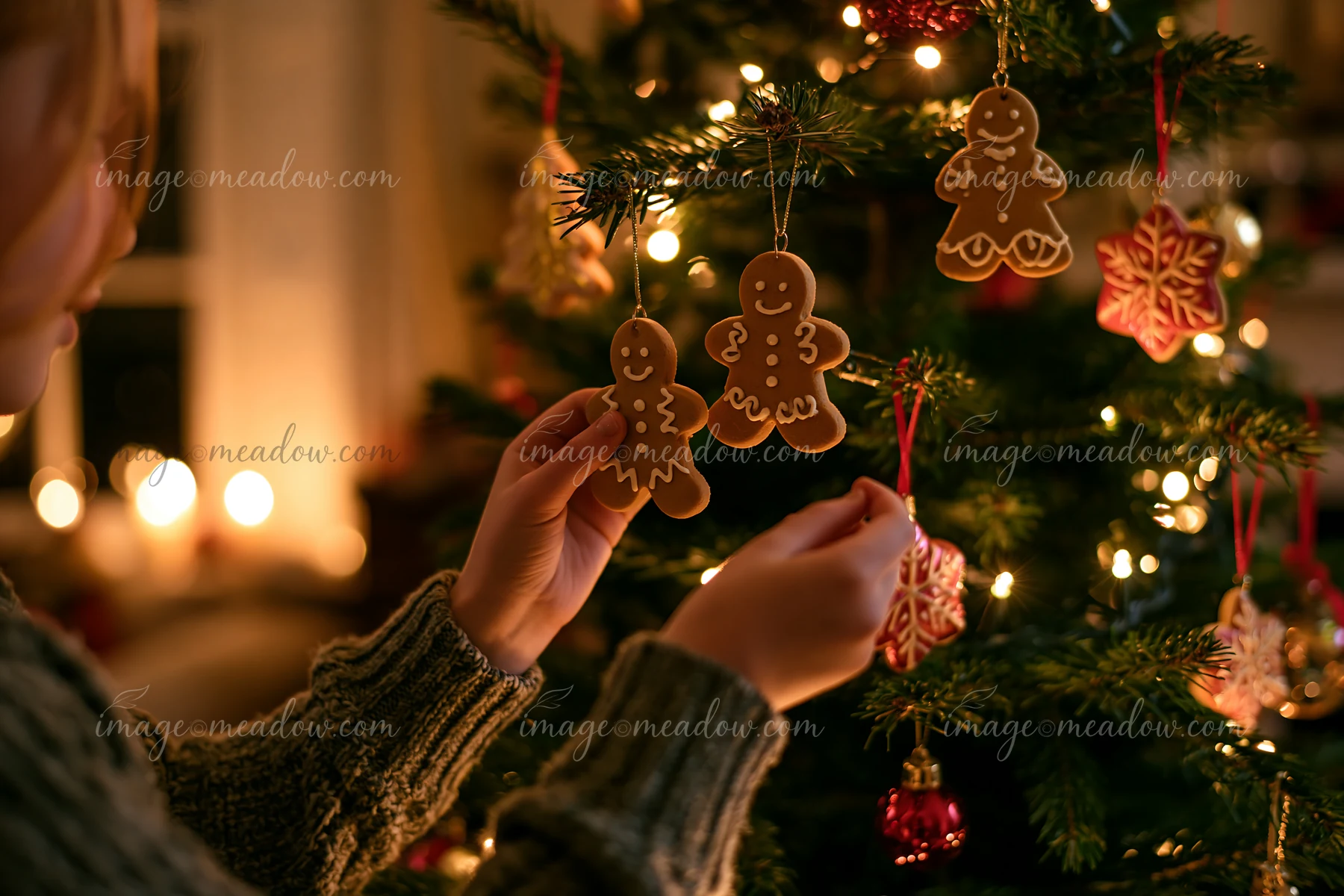A person decorates a Christmas tree with gingerbread ornaments in a cozy living room.