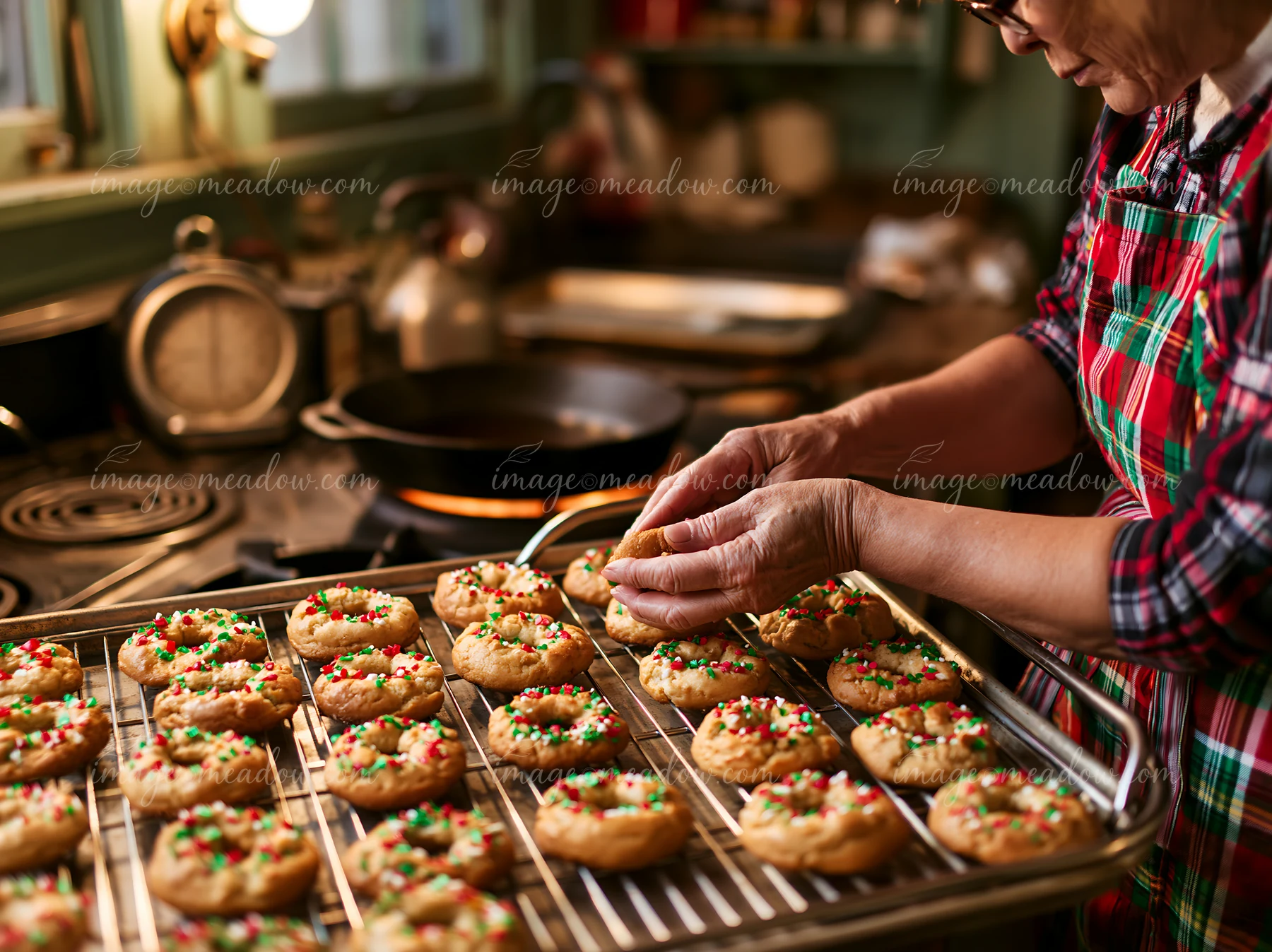 A person decorates freshly baked Christmas cookies with sprinkles in a cozy kitchen.