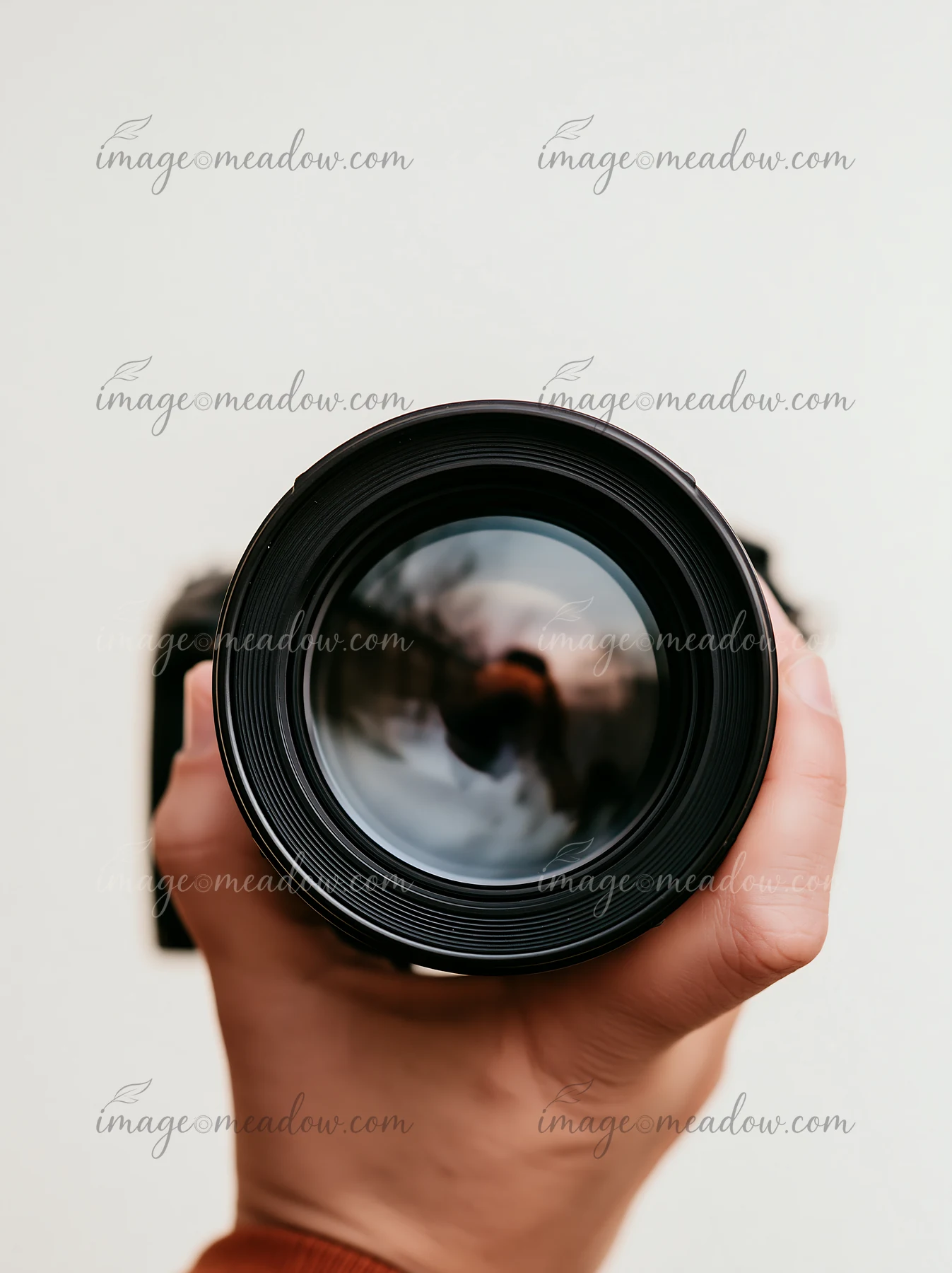 A person holds a camera lens in natural light.