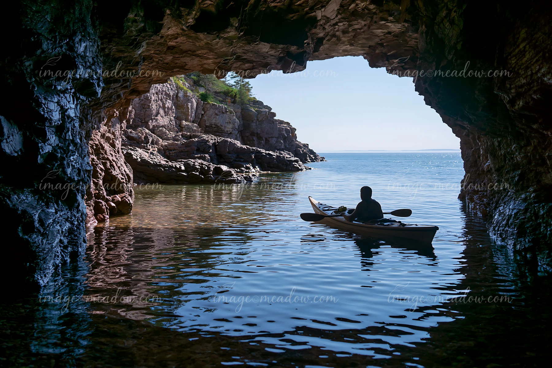 A person in a kayak explores a sea cave, looking out at the coastline.