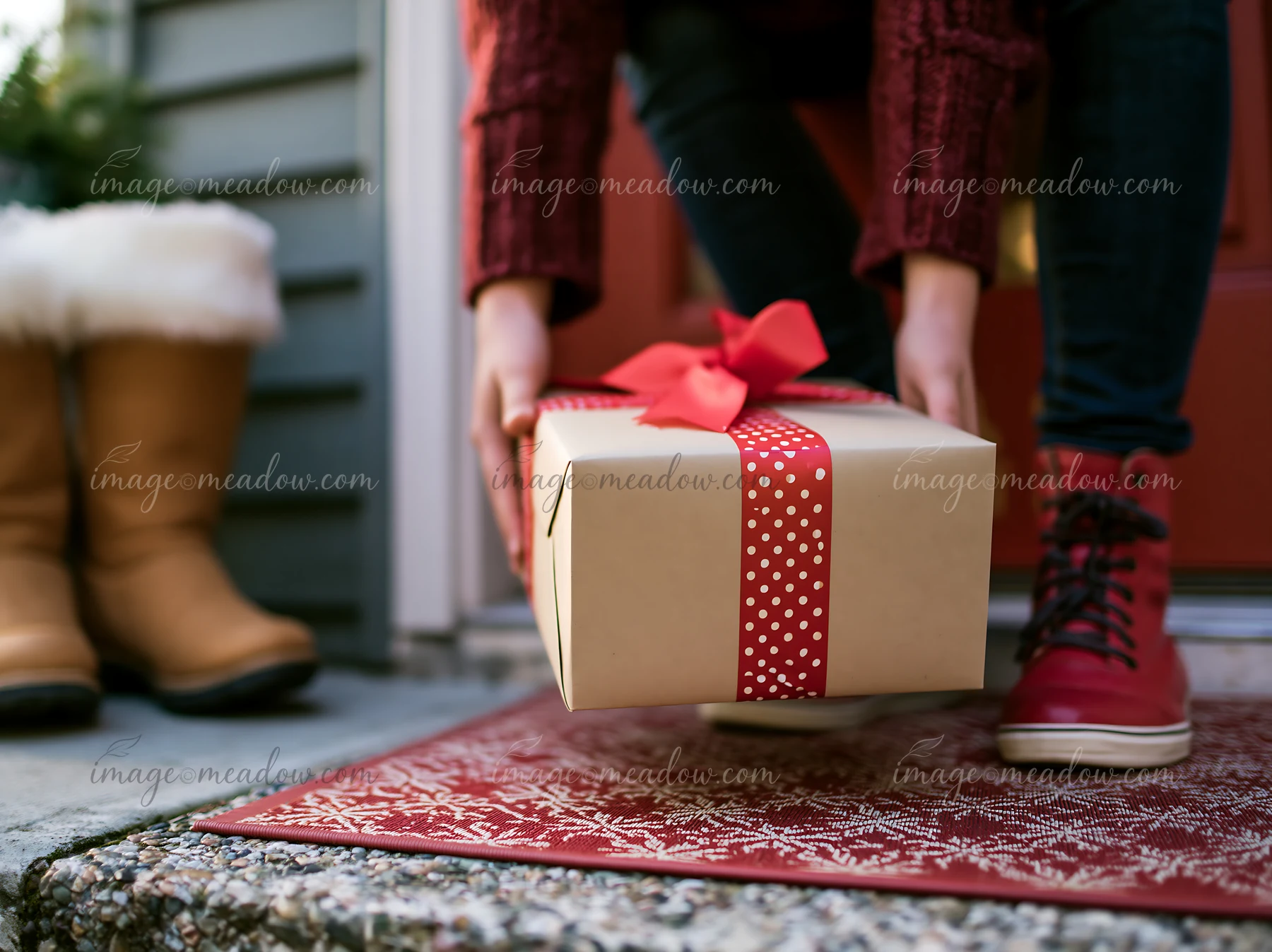 A person is placing a wrapped Christmas gift on the doorstep of a home.