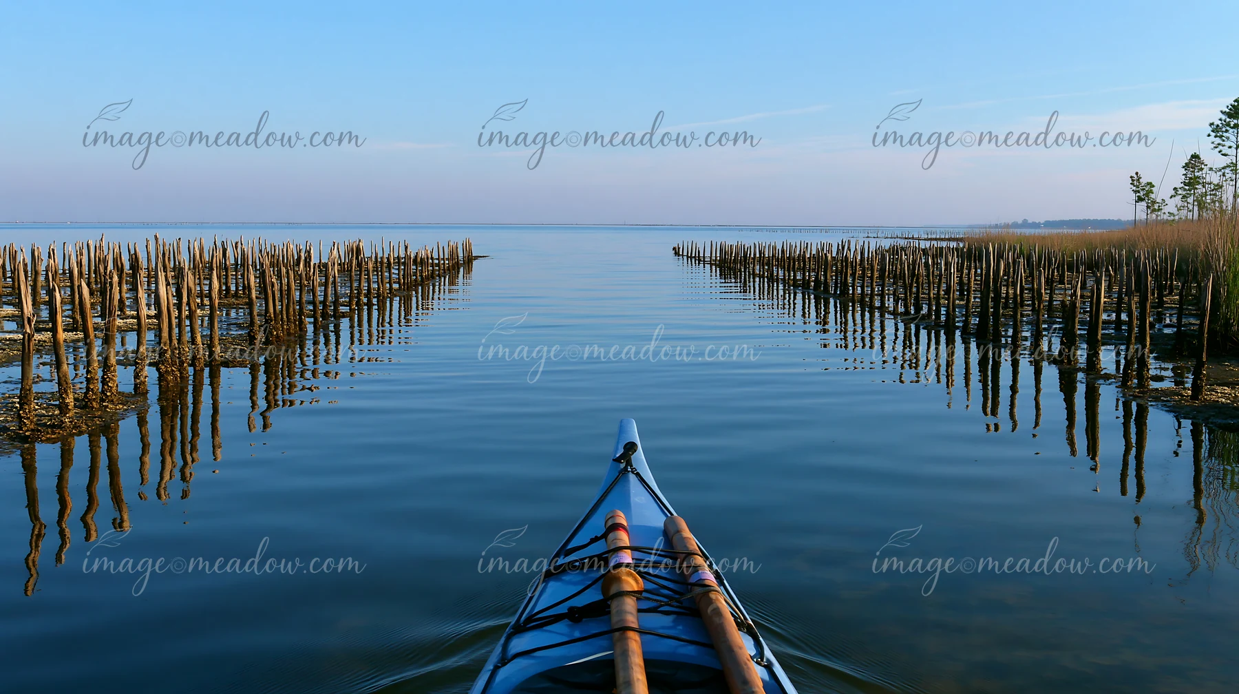A person kayaks through calm water surrounded by wooden structures.