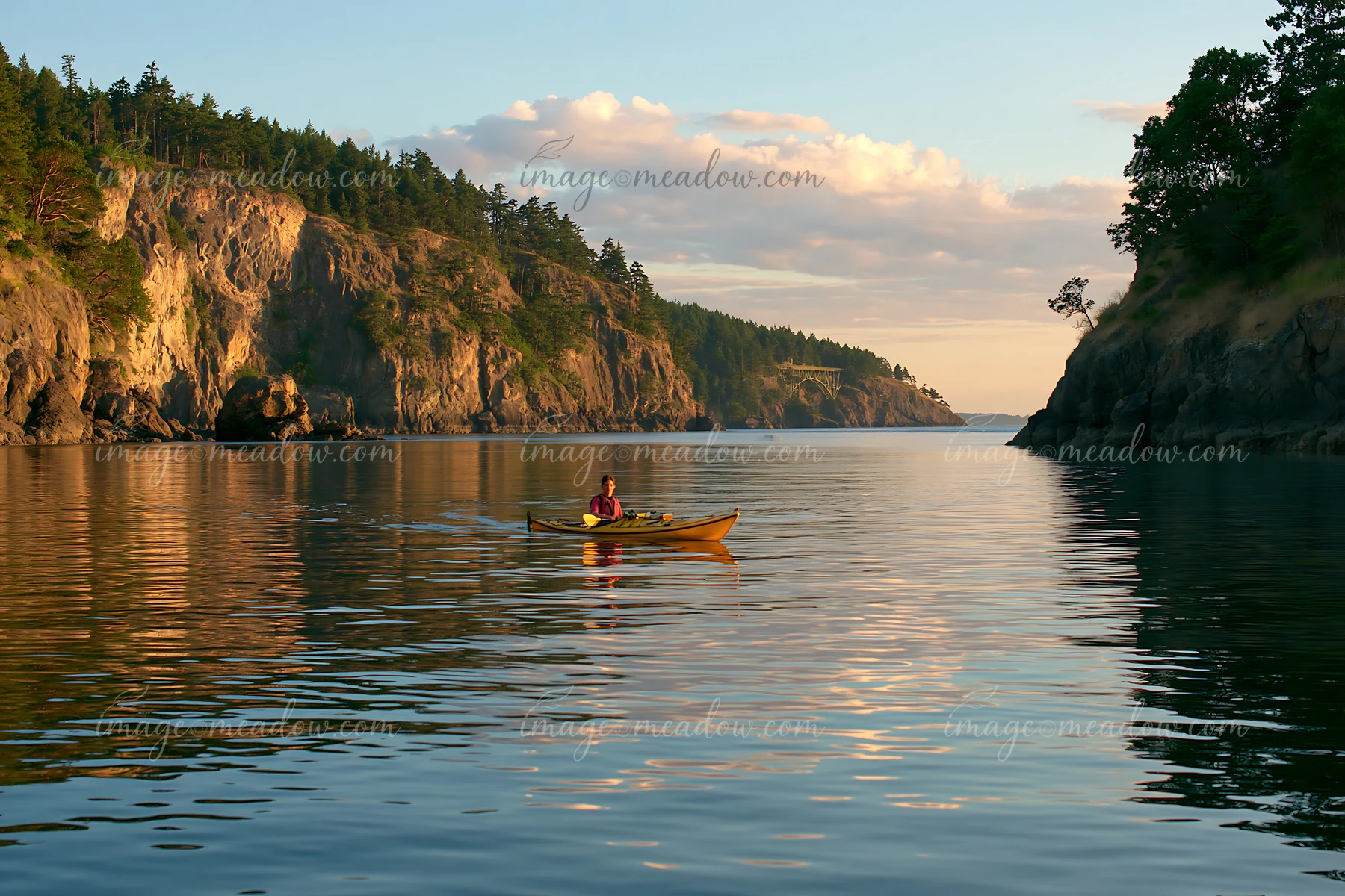 A person paddles a kayak in a sheltered bay surrounded by rocky cliffs and trees.