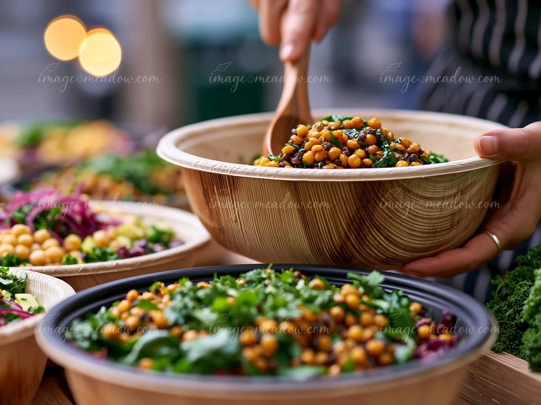 A person serves a salad from a wooden bowl at a buffet set up outdoors.
