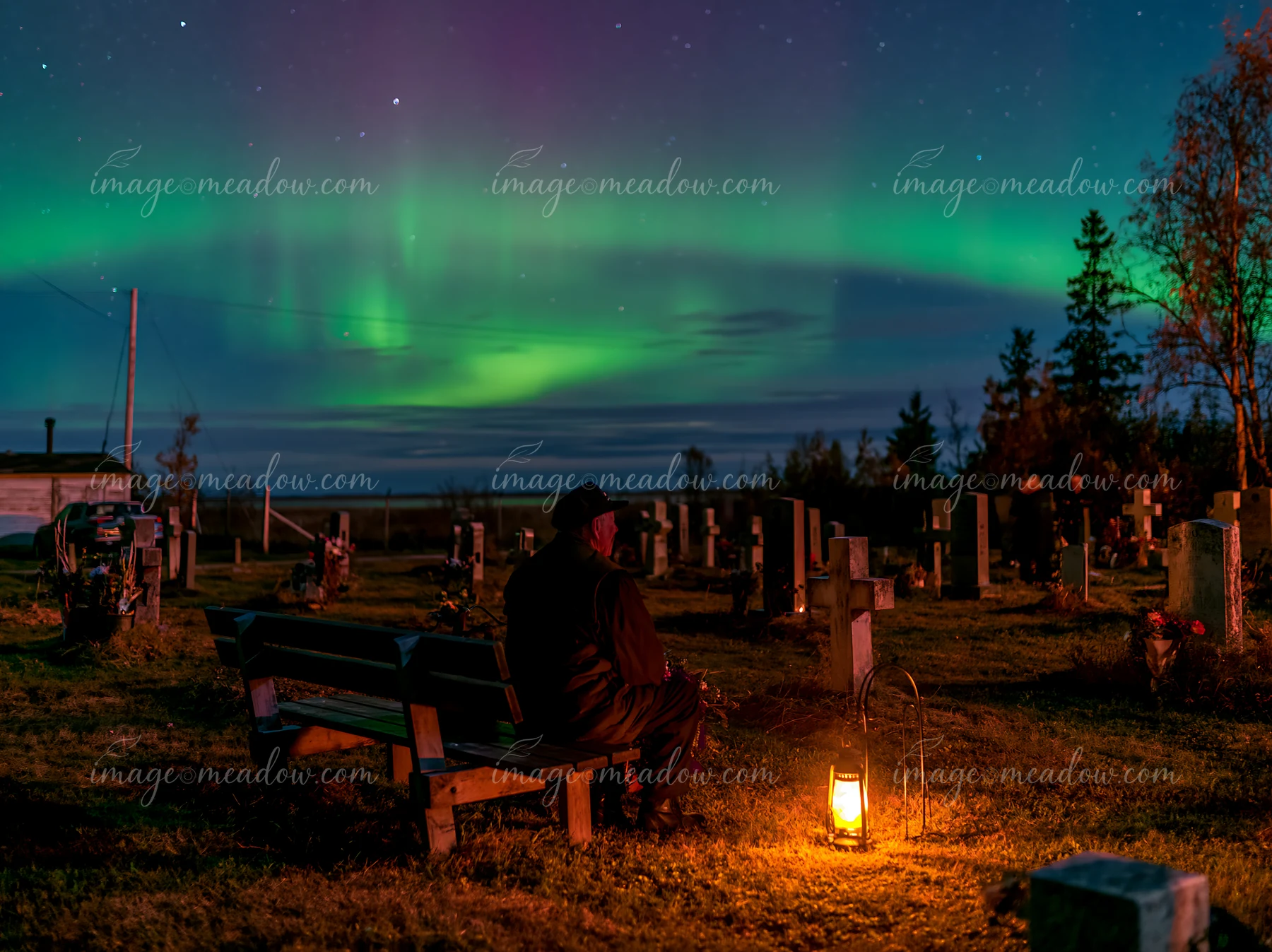A person sits on a bench in a military cemetery under the northern lights.
