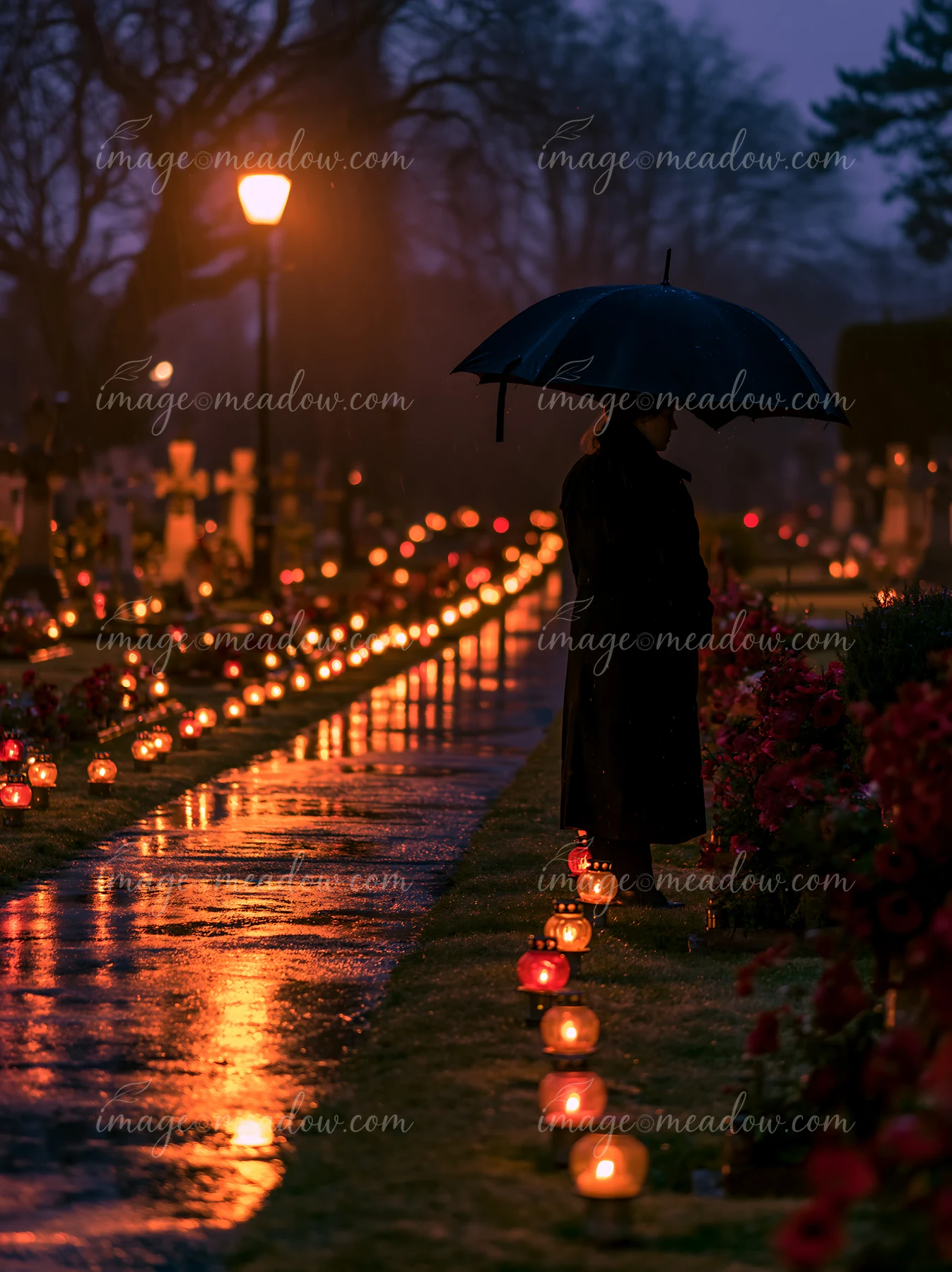 A person stands under an umbrella at a war cemetery during nighttime remembrance.