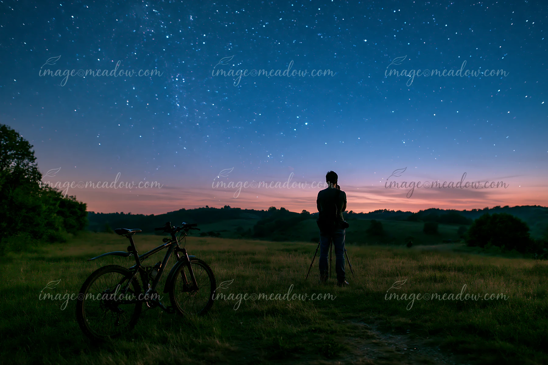 A person stands with a tripod looking at the starry sky in a rural area.