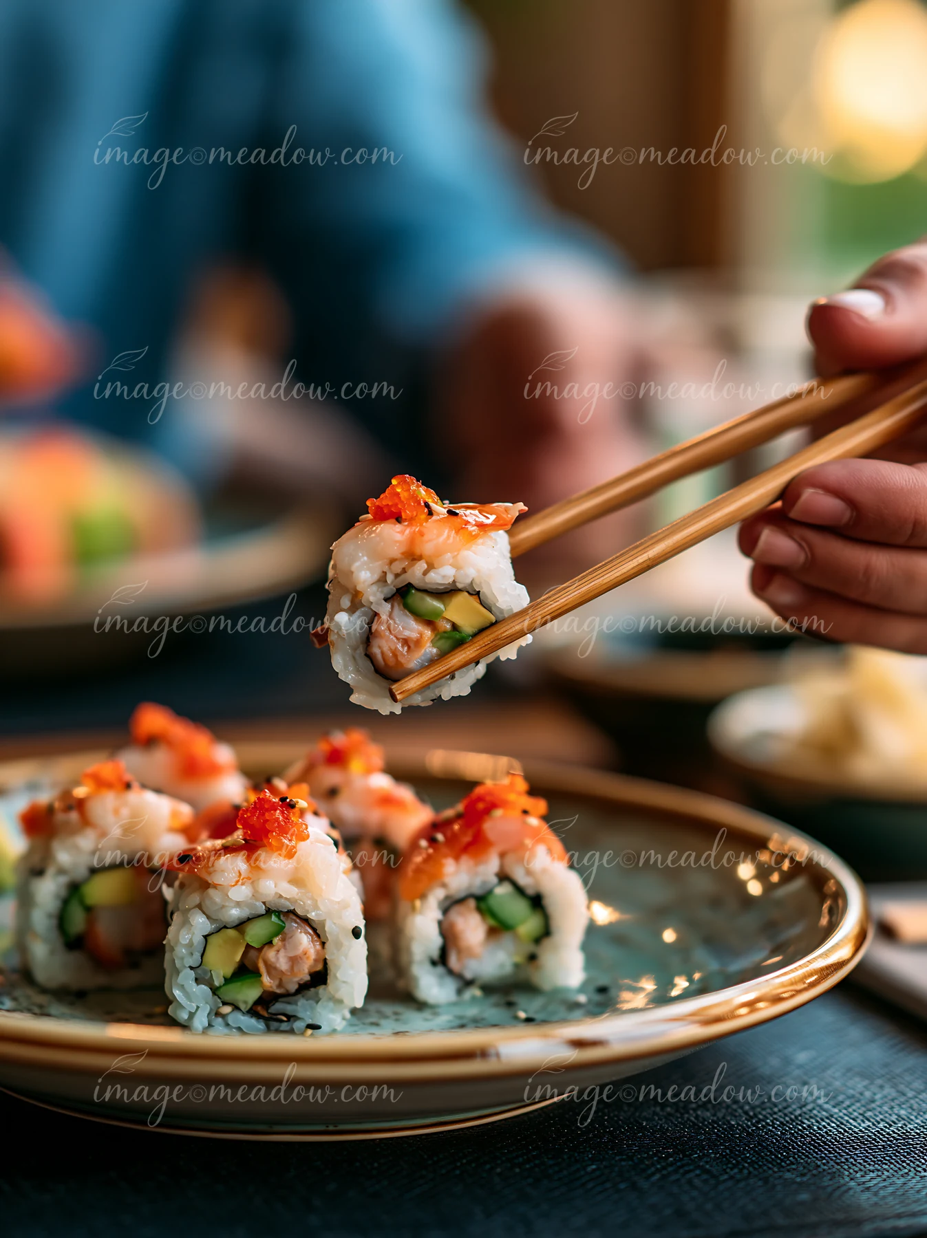 A person uses chopsticks to pick up a sushi roll from a plate.