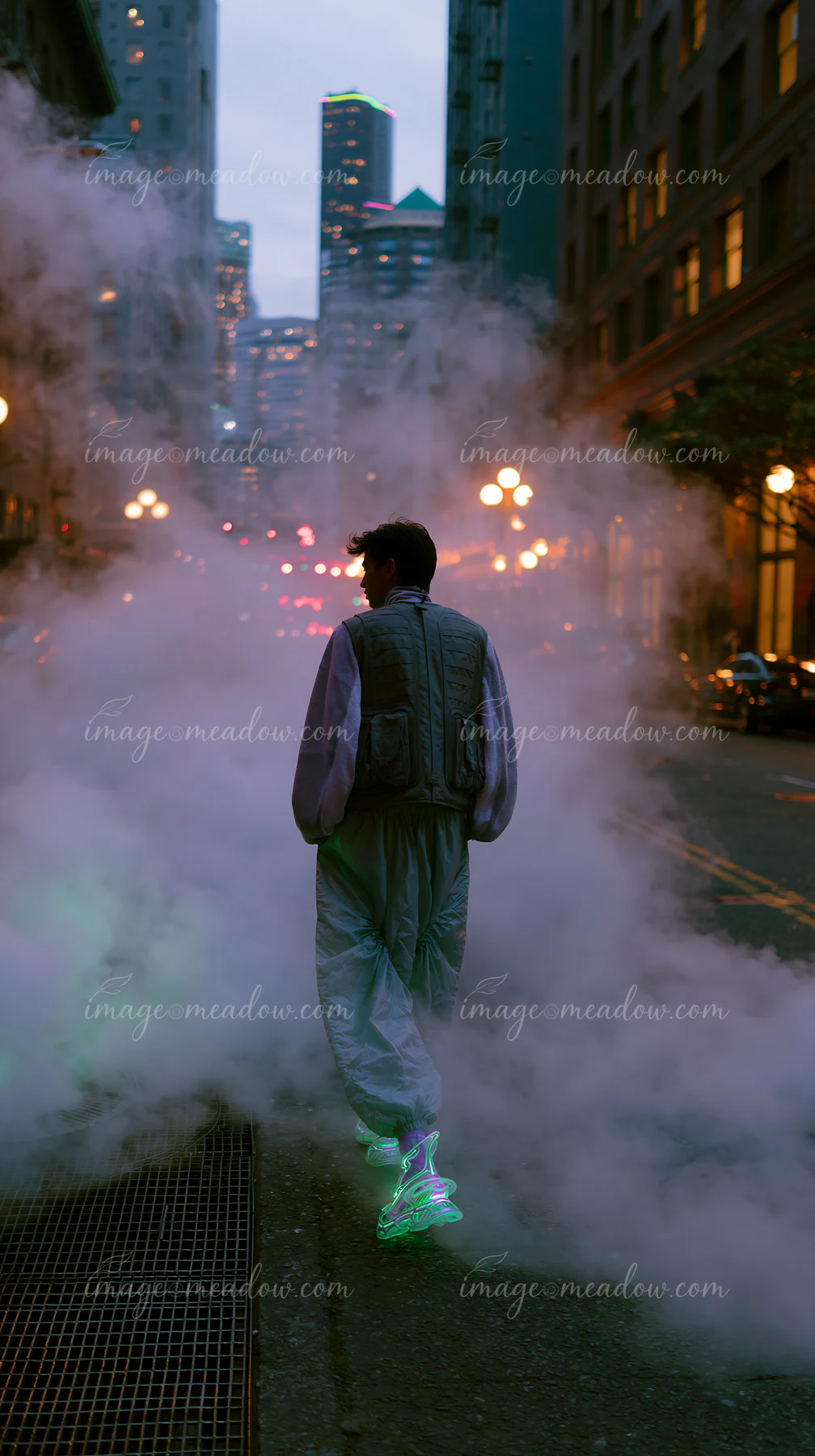 A person walks down a city street enveloped in fog as lights illuminate the buildings.