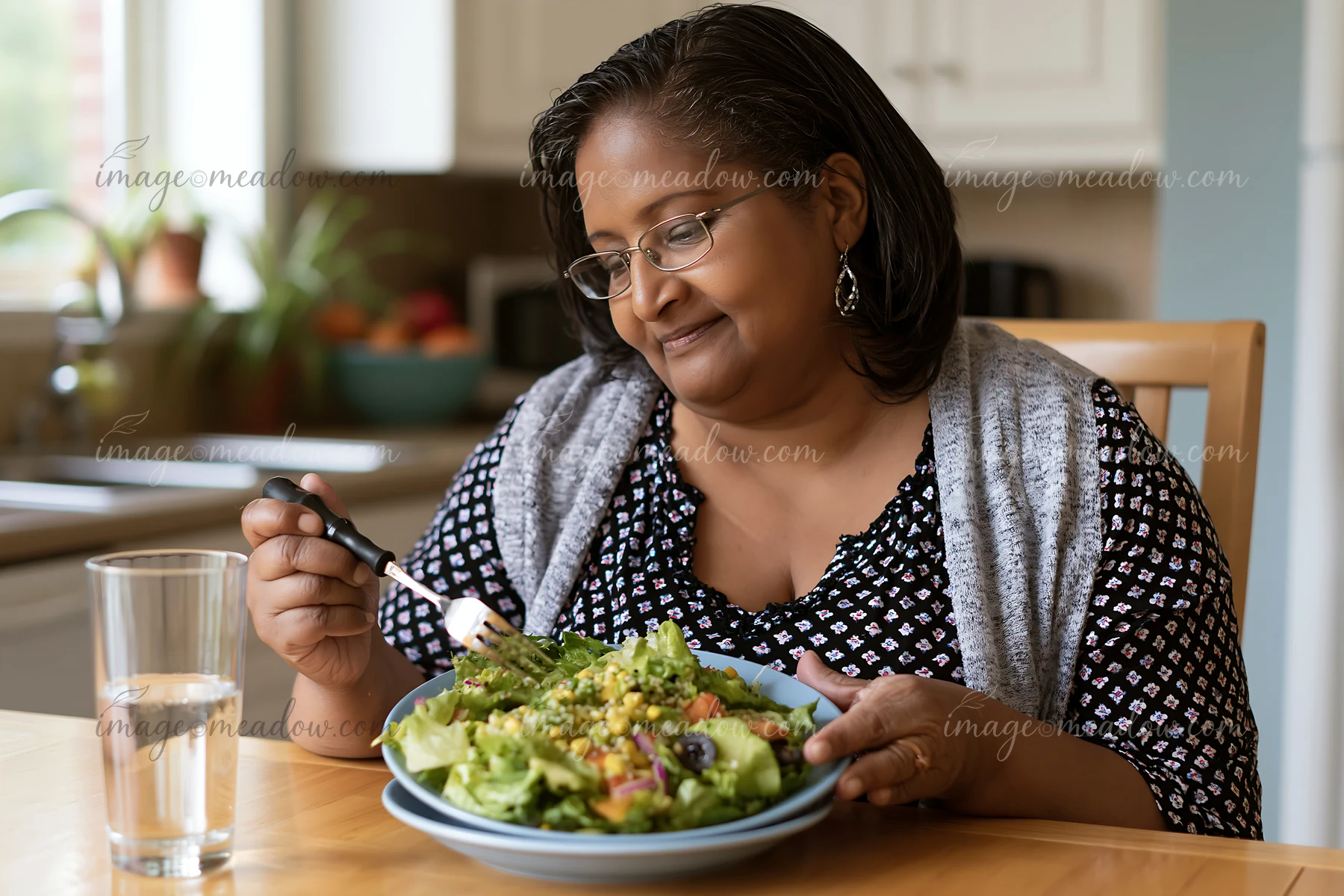 A person with limited hand mobility using utensils enjoys a large salad in a kitchen.