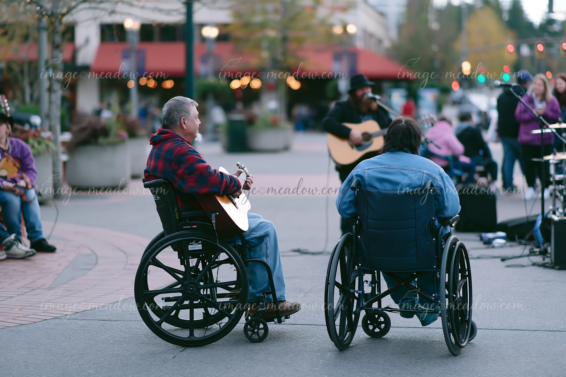A person with muscular dystrophy using a wheelchair enjoys a live music performance in a busy outdoor setting.