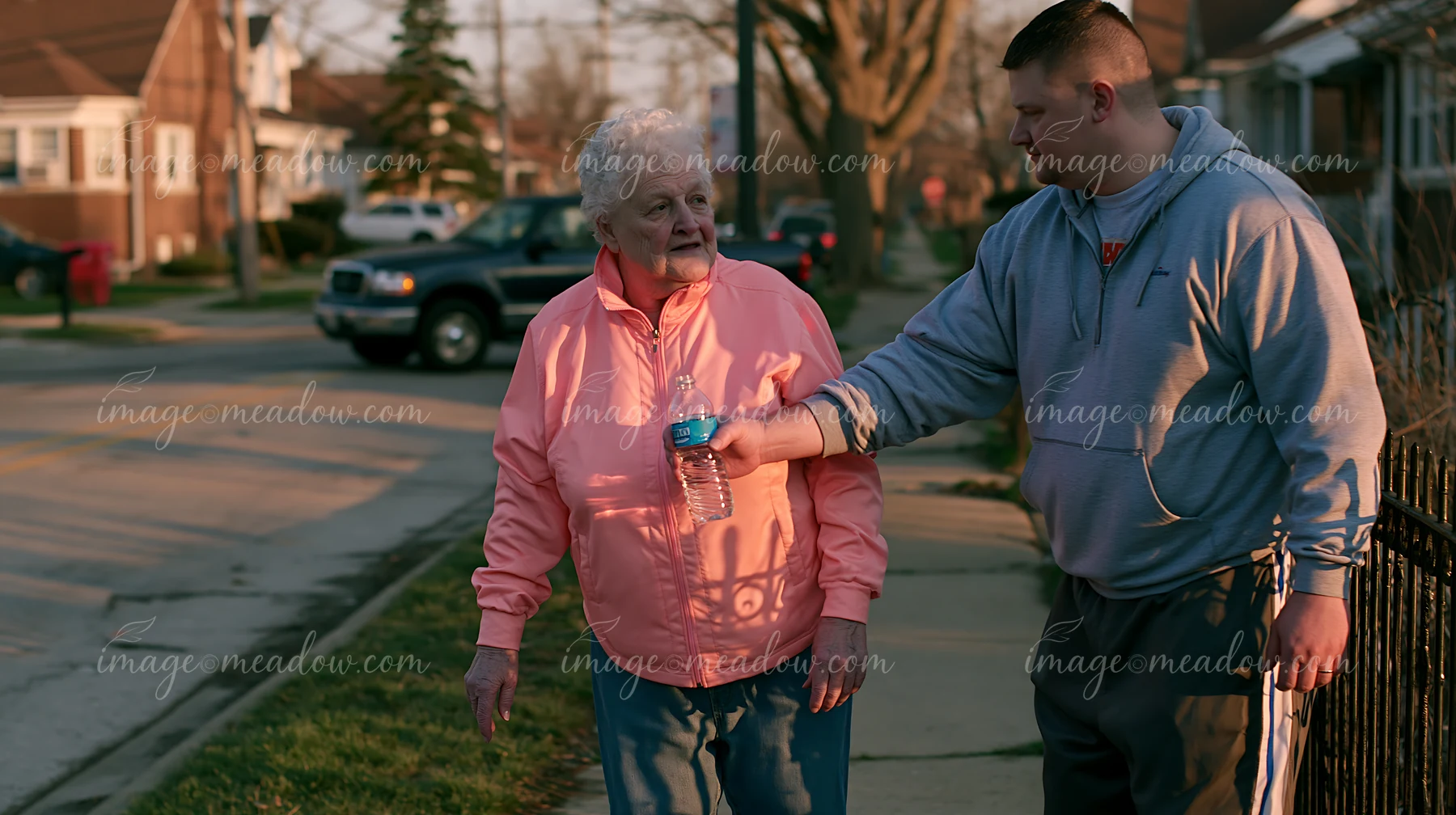 A person with Parkinson's disease receiving support from a caregiver while walking on a neighborhood street.
