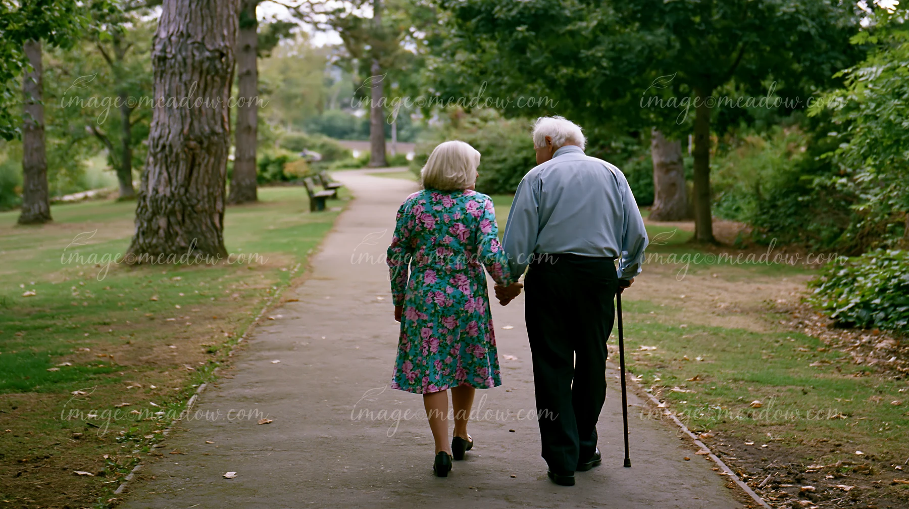 A person with Parkinson's disease receiving support walks hand in hand with a partner in a park.