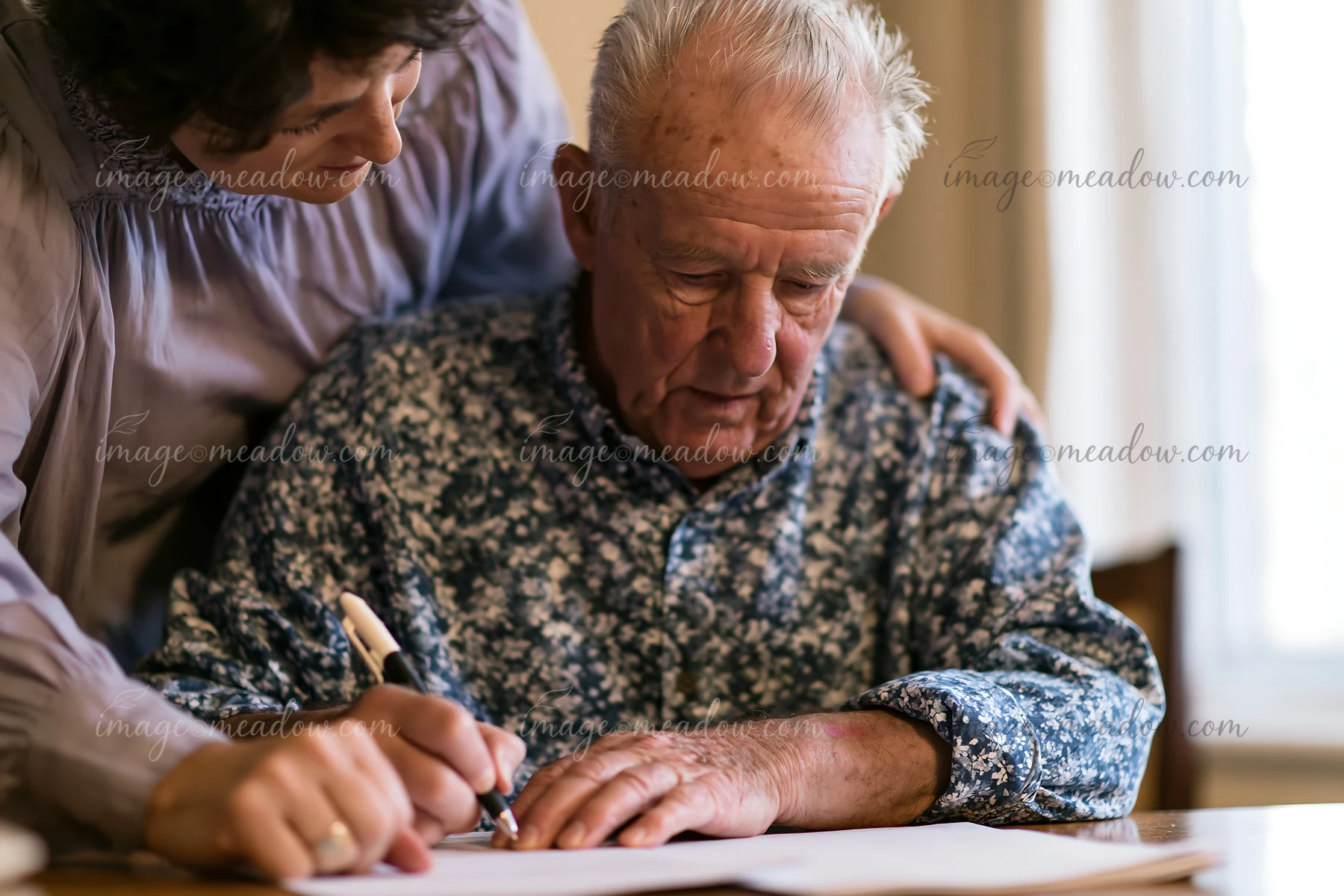 A person with Parkinson's disease receiving support while writing at a table.