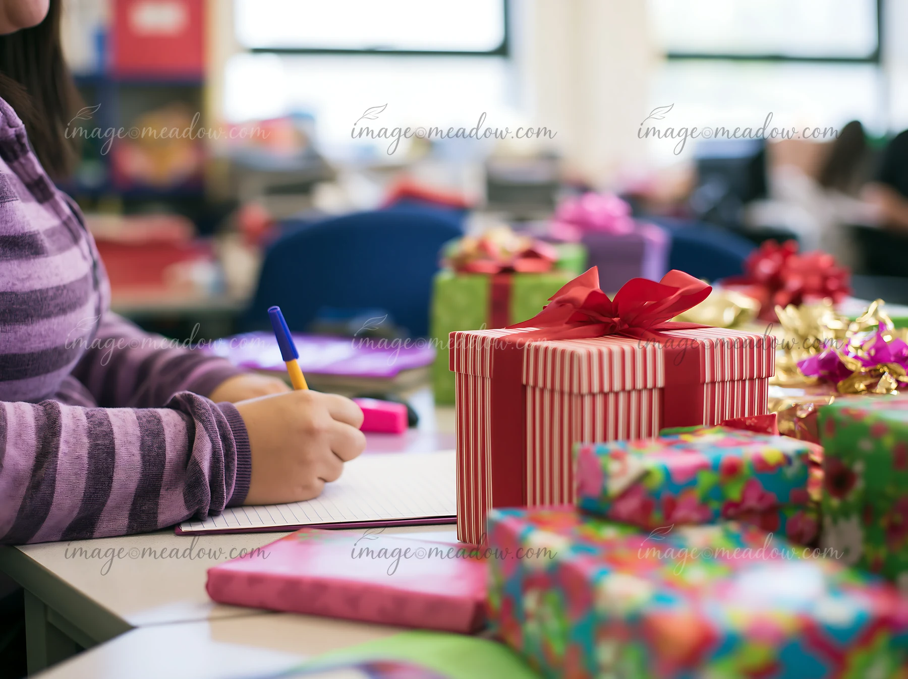 A person writes a gift list at a desk surrounded by colorful wrapped presents.